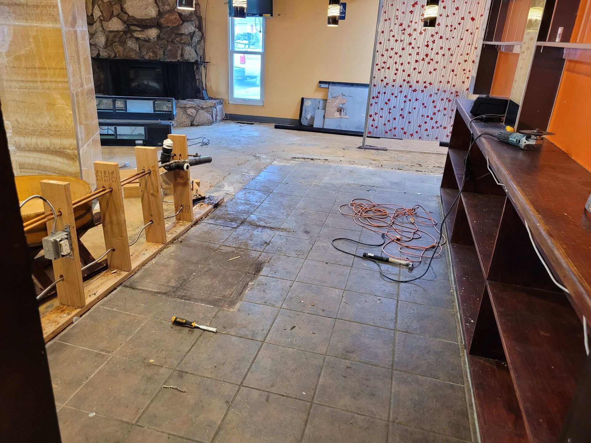 Empty, partially demolished room with broken floor tiles, exposed stone wall, and scattered debris.