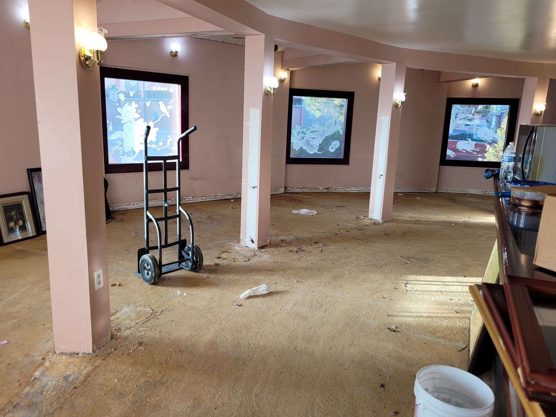 Empty room under renovation with pink columns, debris on the floor, and windows letting in daylight