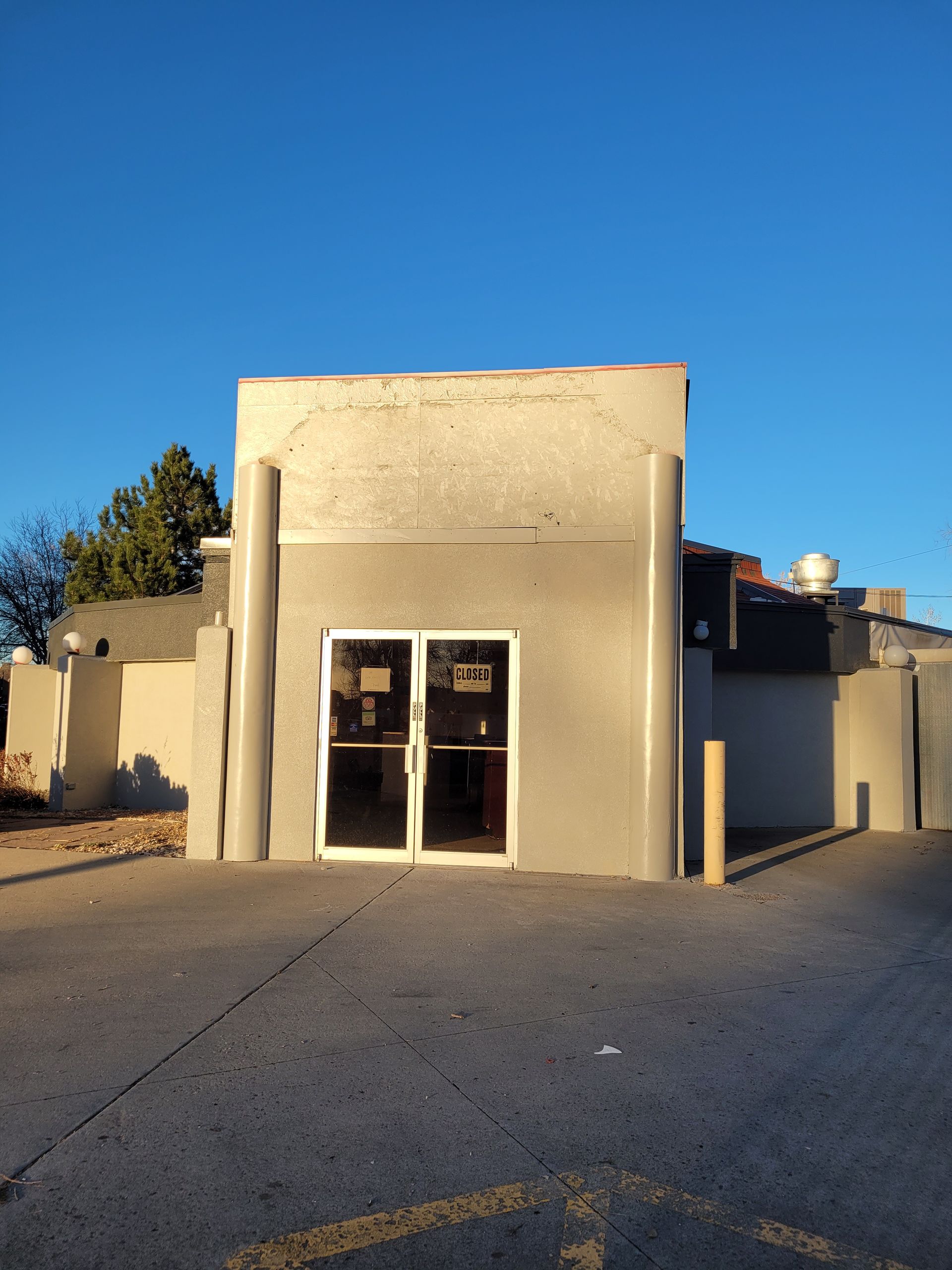 Small beige building with glass doors under a clear blue sky, viewed from a paved lot