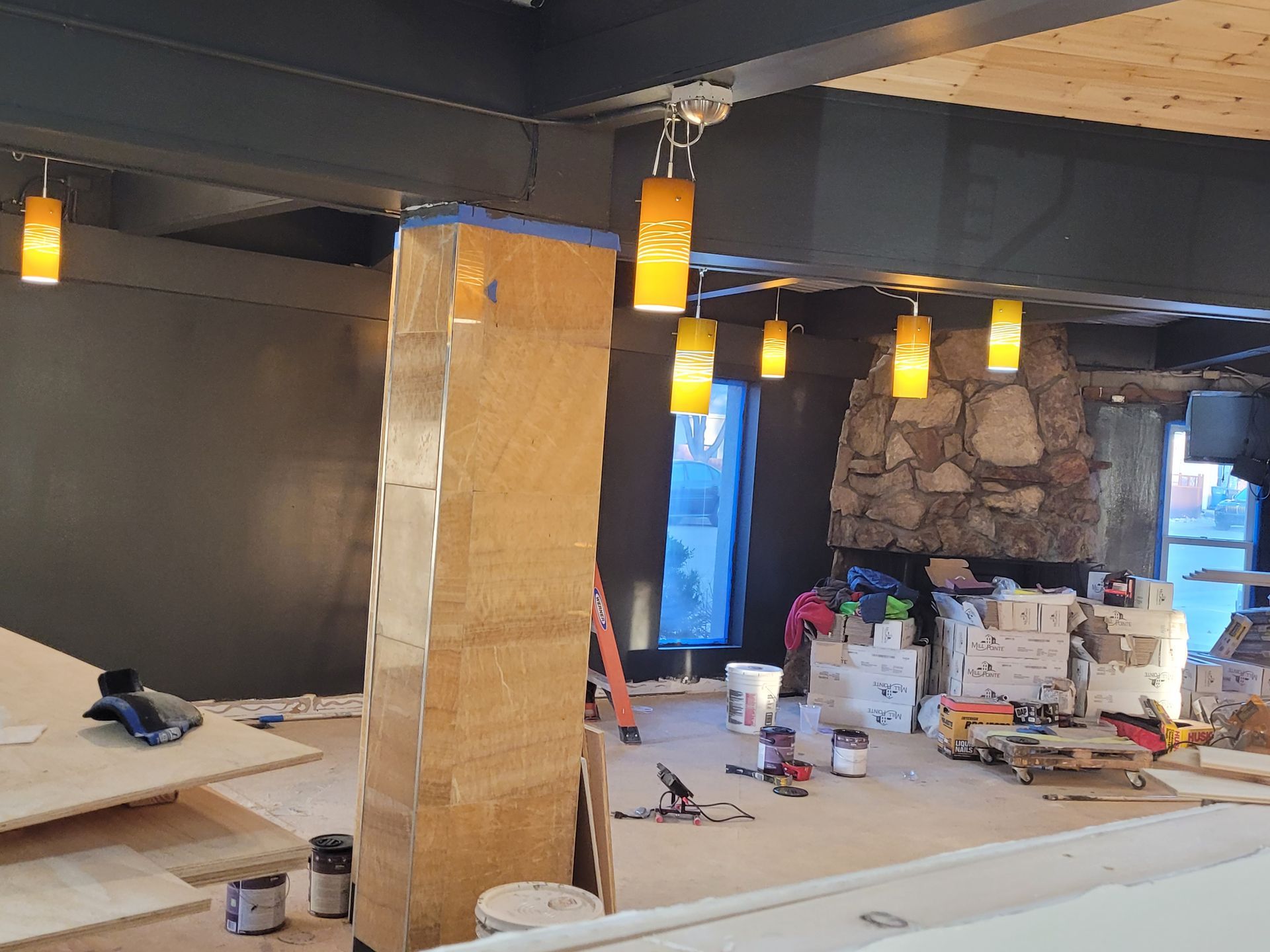 Renovated room with exposed stone pillar, hanging pendant lights, and construction tools on the floor