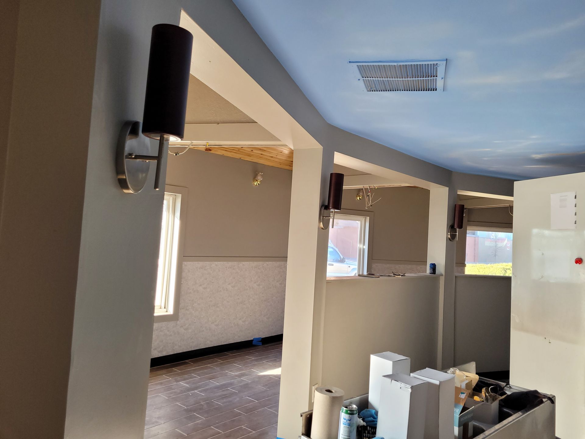 Empty room with beige walls, exposed beams, and construction materials near windows and a wall light.