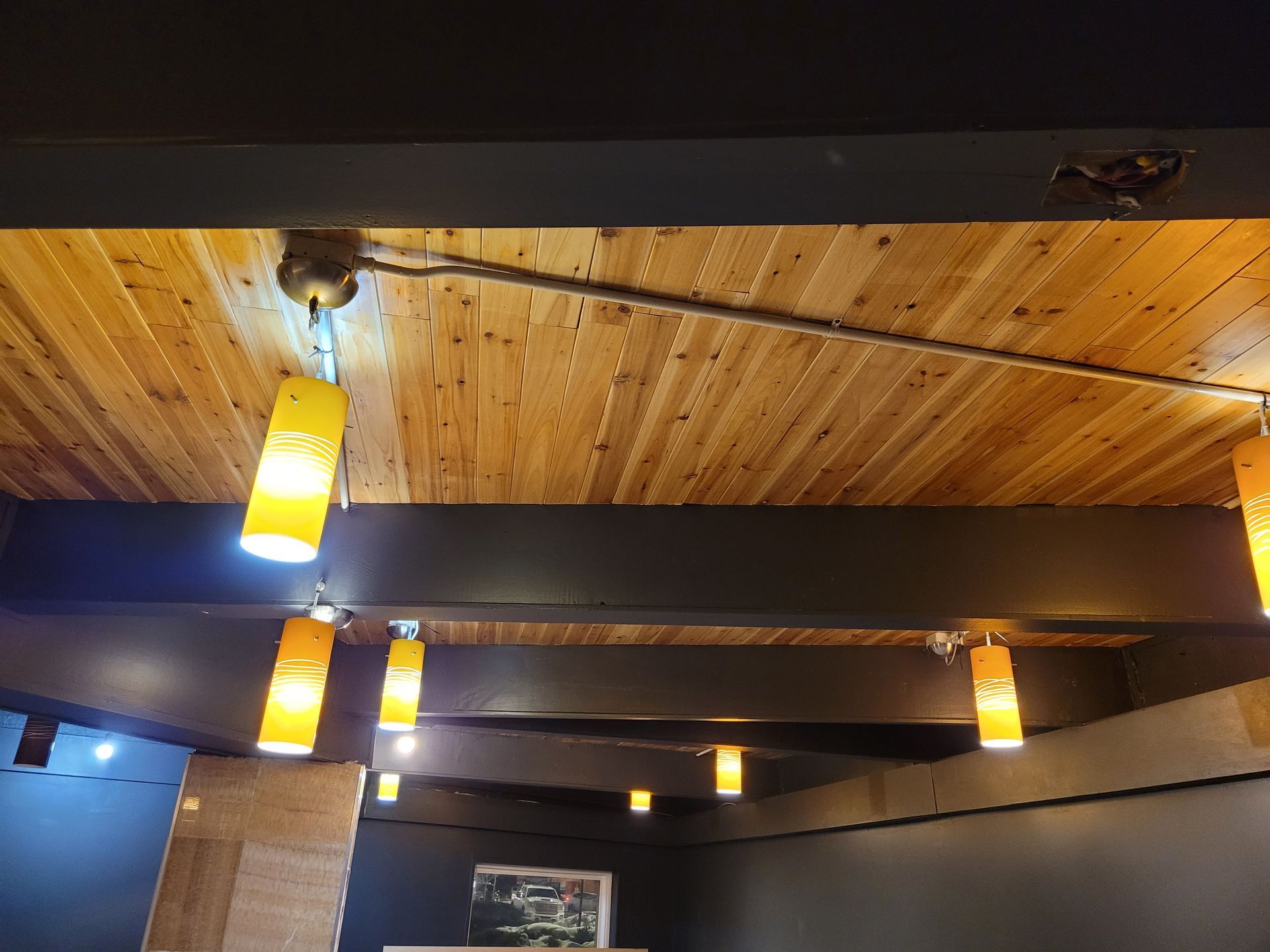 Wood-paneled ceiling with exposed dark beams and hanging yellow pendant lights in a room
