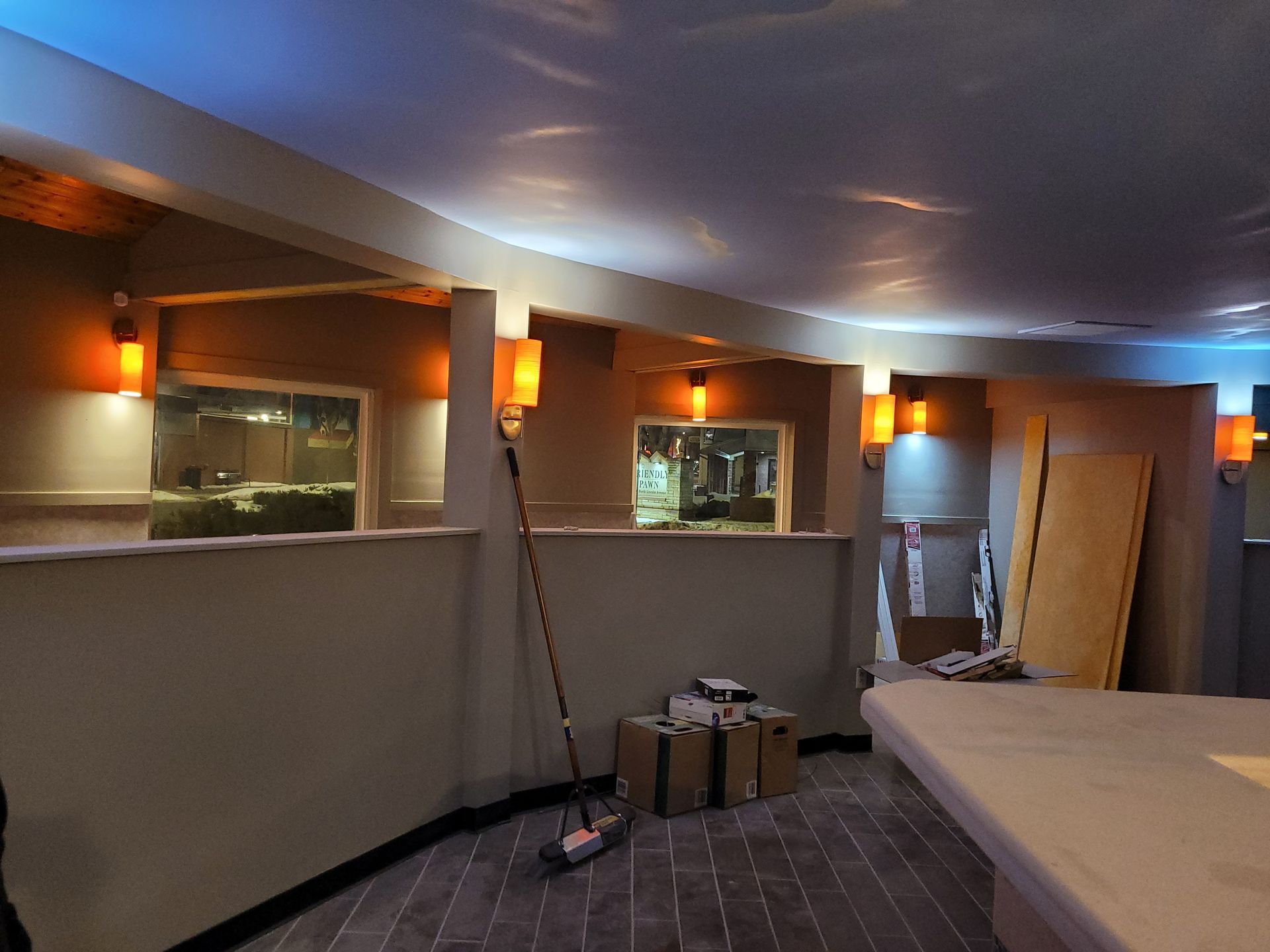 Unfinished room with curved white ceiling, wall sconces, windows, and construction materials on the floor and table.