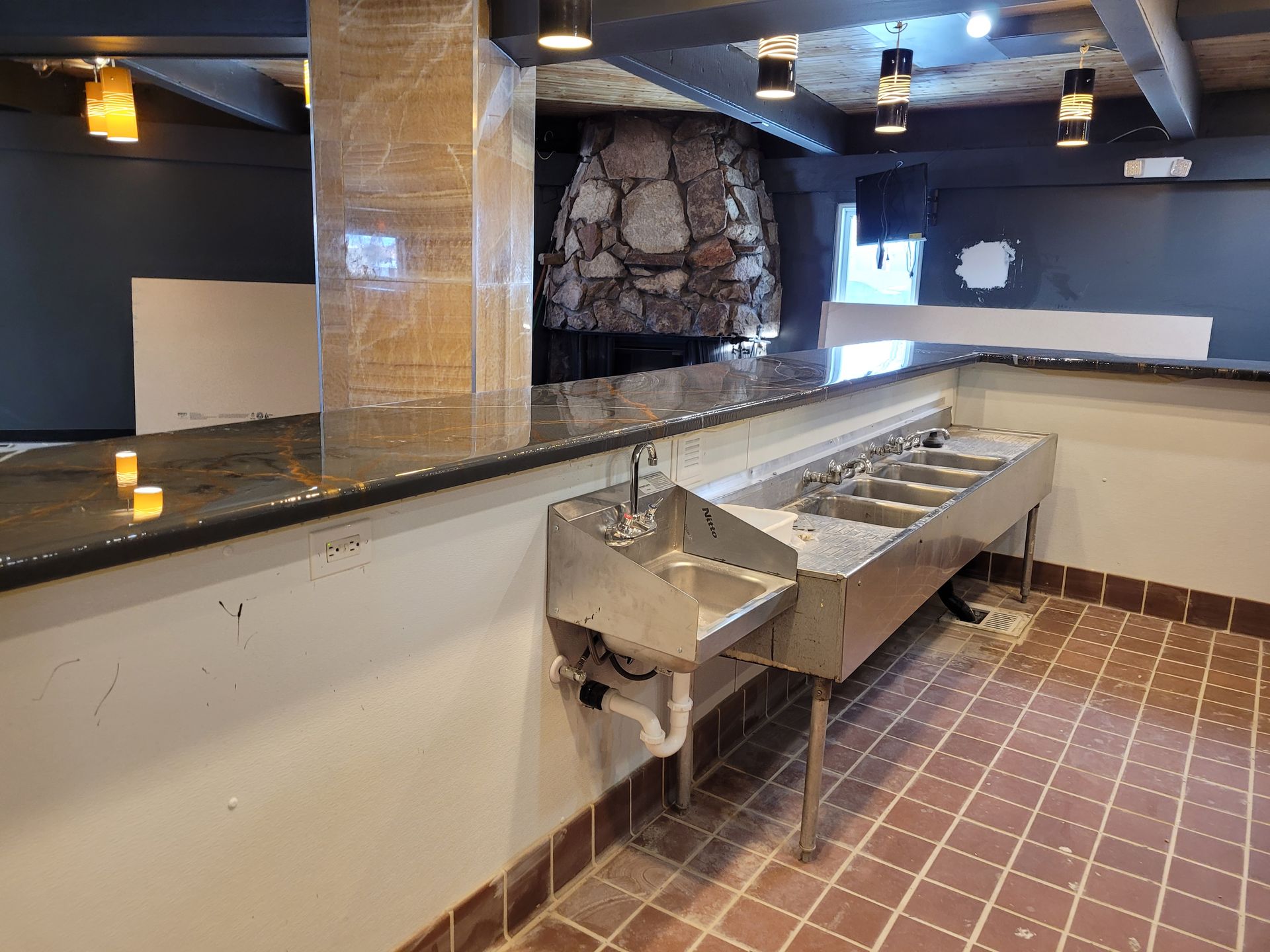 Empty restaurant bar with sinks, black countertop, tiled floor, and stone fireplace in back room