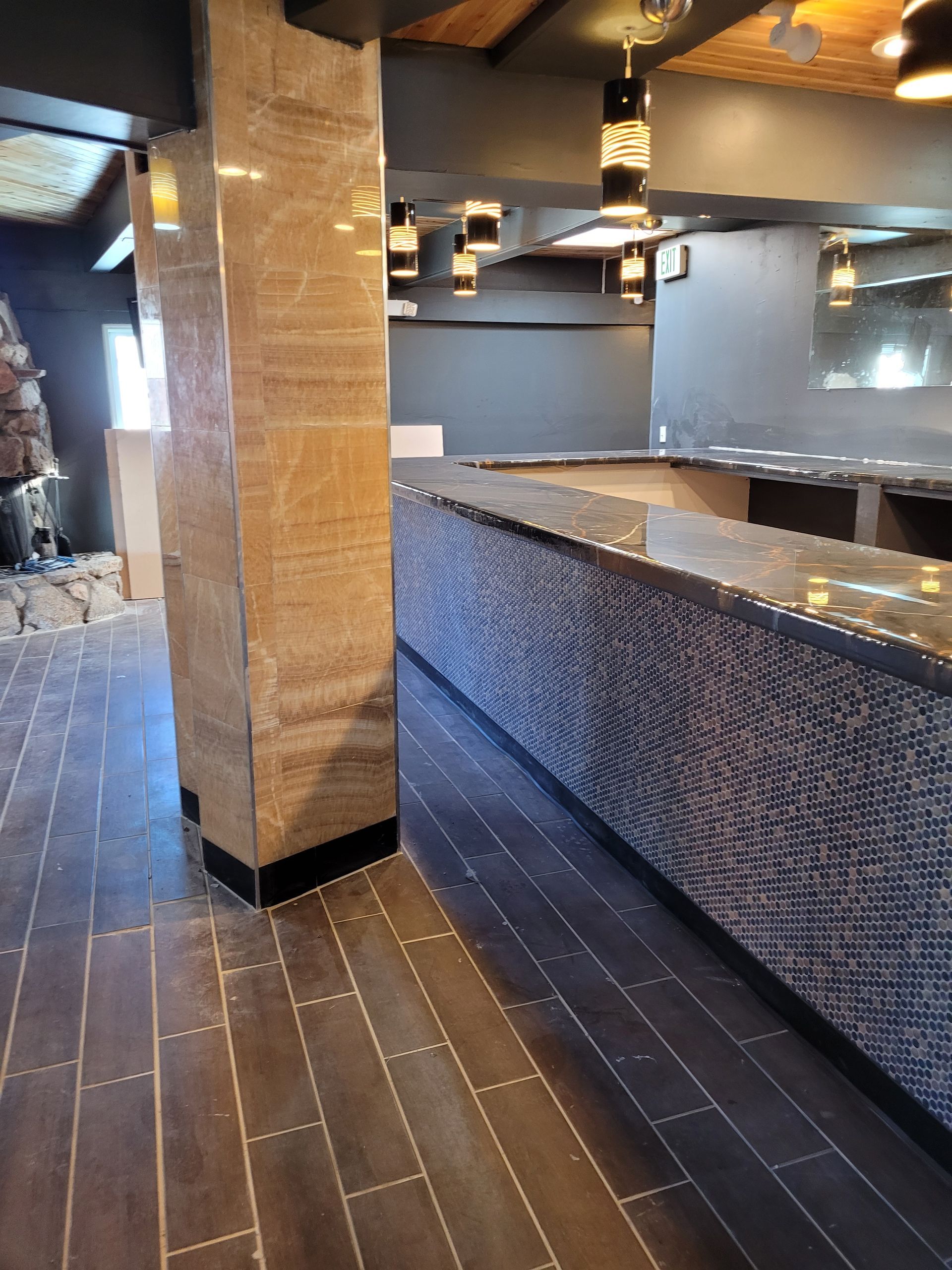 Empty modern bar interior with dark tile floors, wood beams, and a mosaic-tiled counter