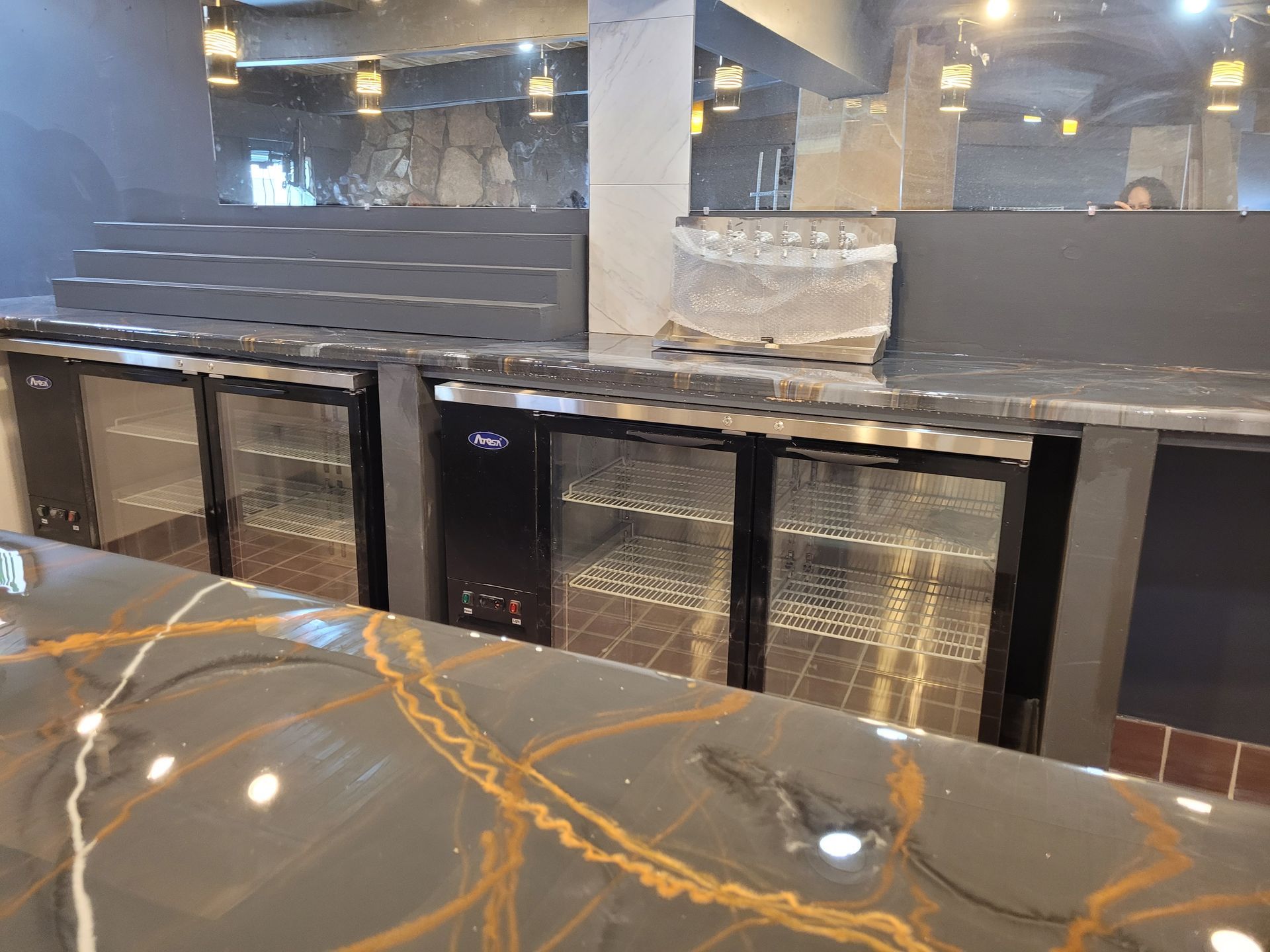 Bar with glossy black countertop, under-counter refrigerators, and stacked clear ice in a modern interior