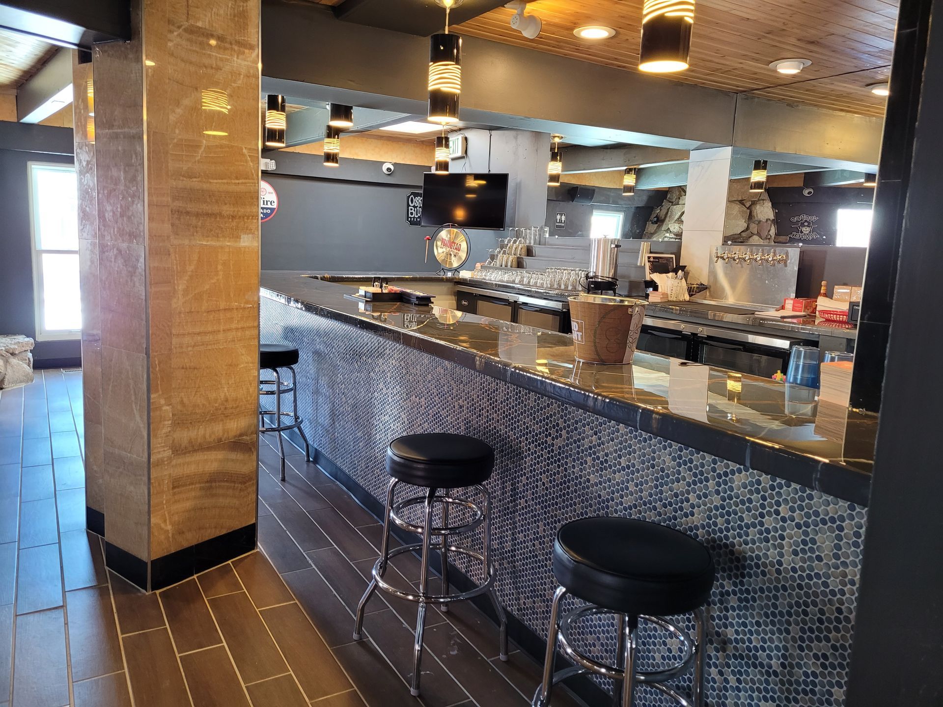 Empty restaurant bar with brown tiles, mirrored counter, and two black stools