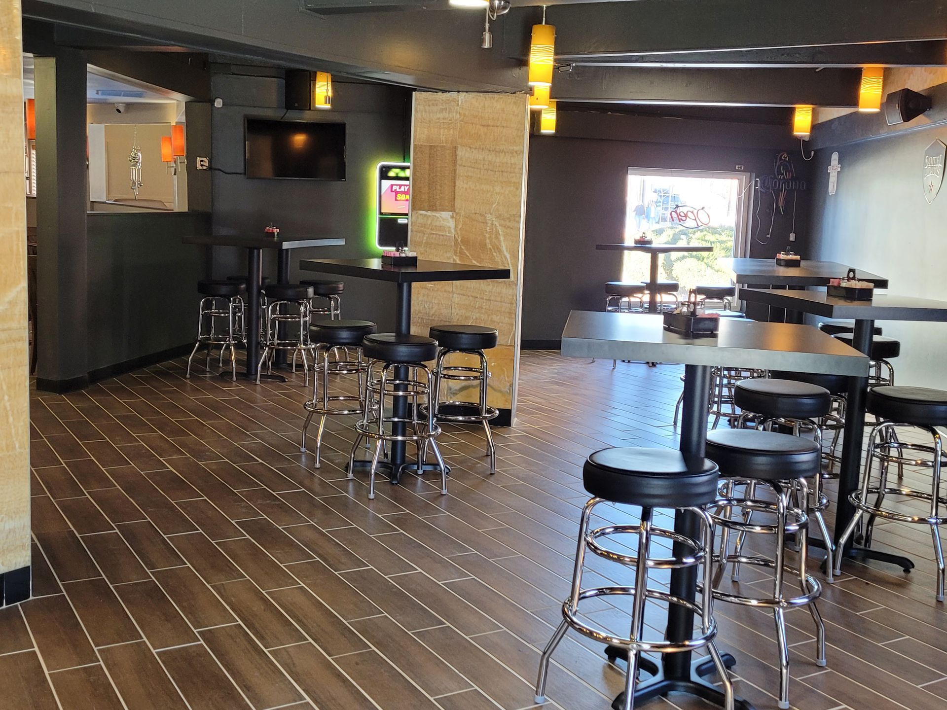 Empty bar interior with black stools, round tables, and dim pendant lights on a tiled floor