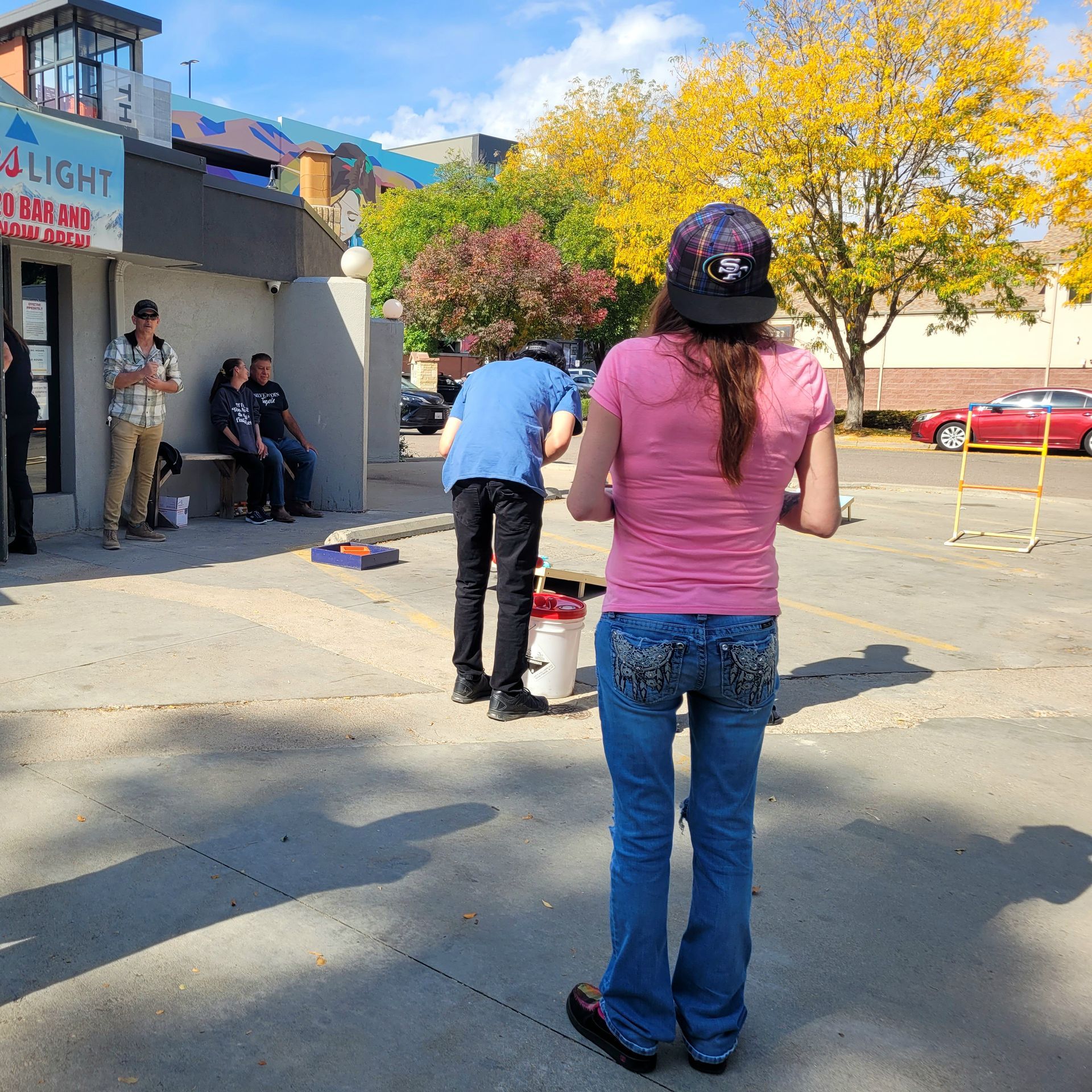 Two people at an outdoor game booth, one lining up a shot toward a target on the ground.