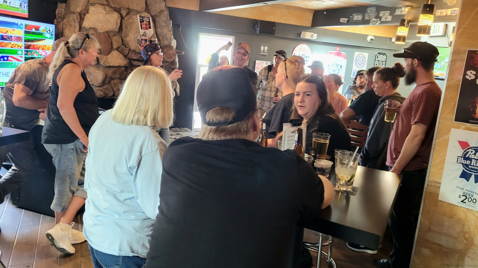 People seated around a table in a busy rustic bar or café, chatting and drinking.