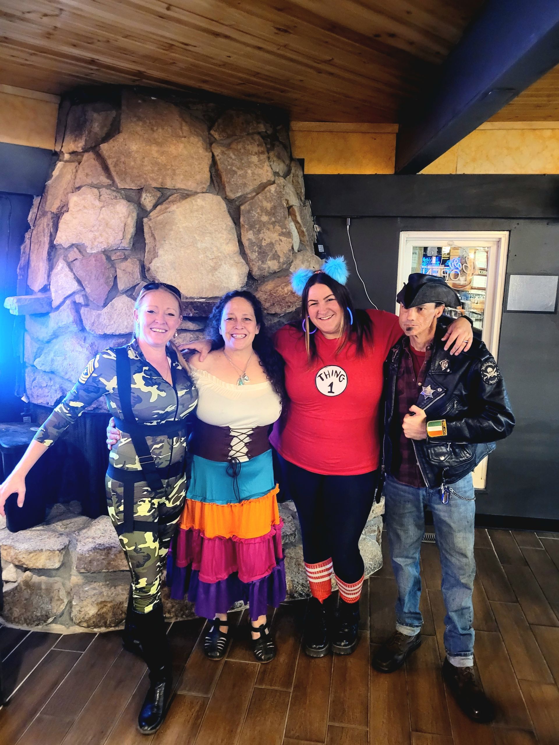 Four people posing indoors by a stone fireplace, smiling in colorful clothes and jackets.