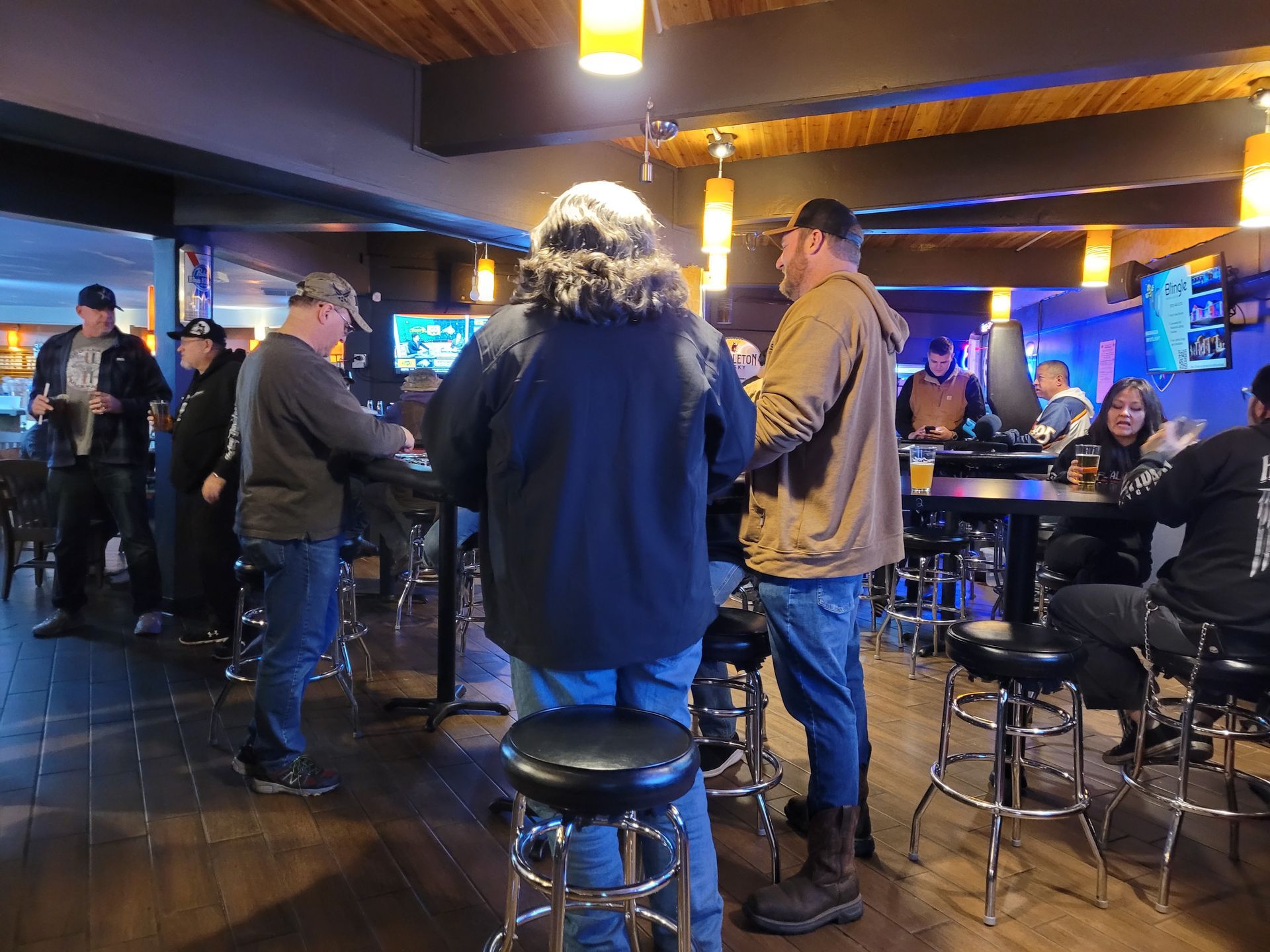 People standing and talking in a dimly lit bar with stools and blue neon lights