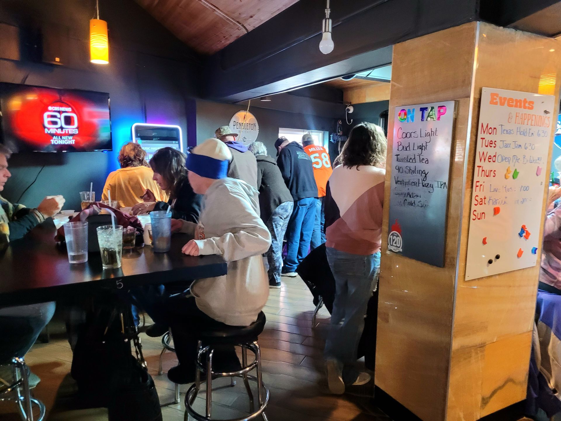 People chatting in a dim bar with neon lights and a chalkboard menu on the wall