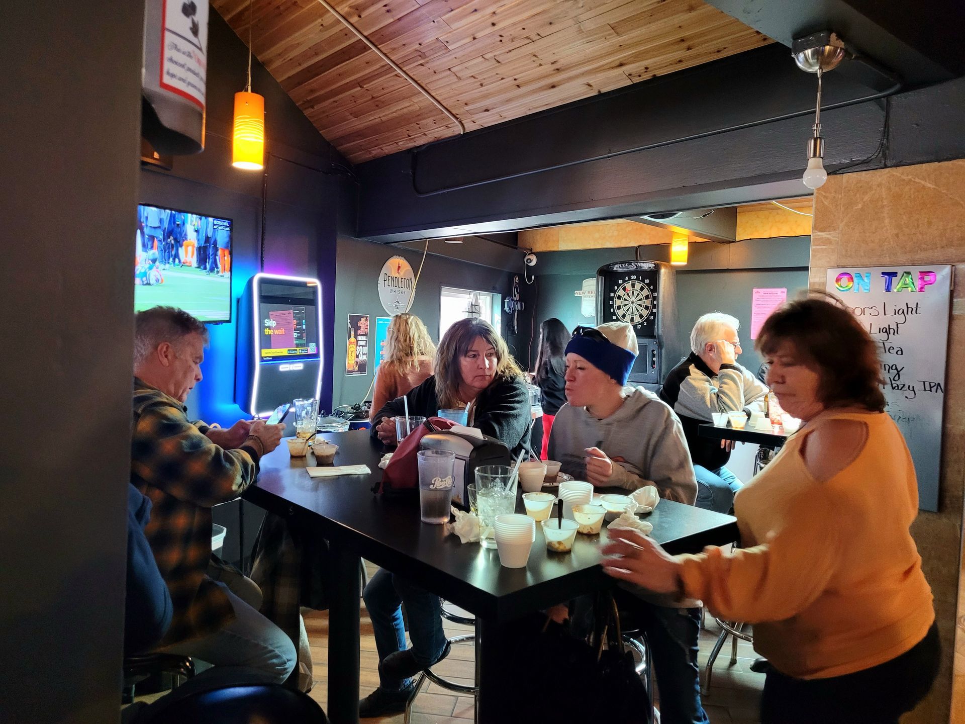 People gathered around a table in a cozy bar, chatting and drinking under warm lights.