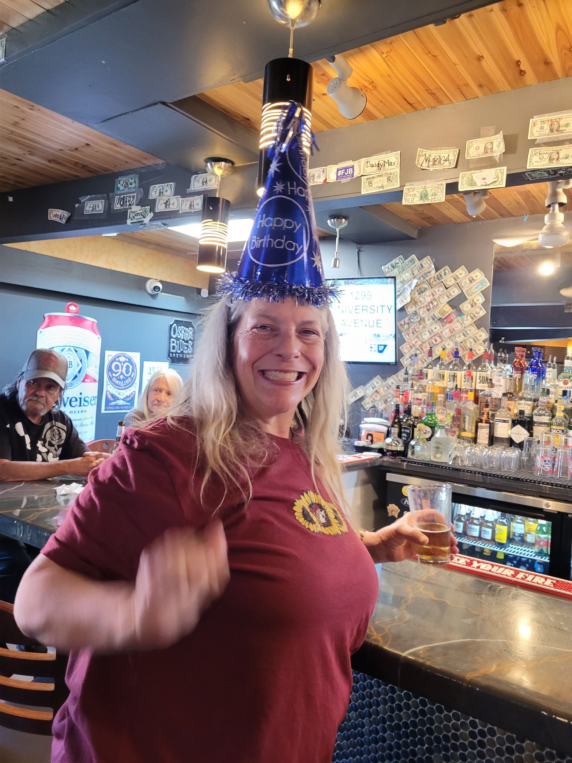 Woman in a blue party hat smiling at a bar with drinks and decorations in the background