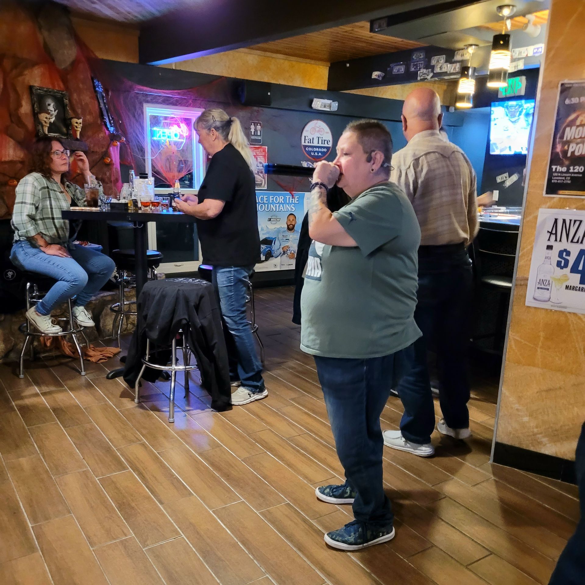 People standing and chatting in a dimly lit bar with wooden floors and neon signs