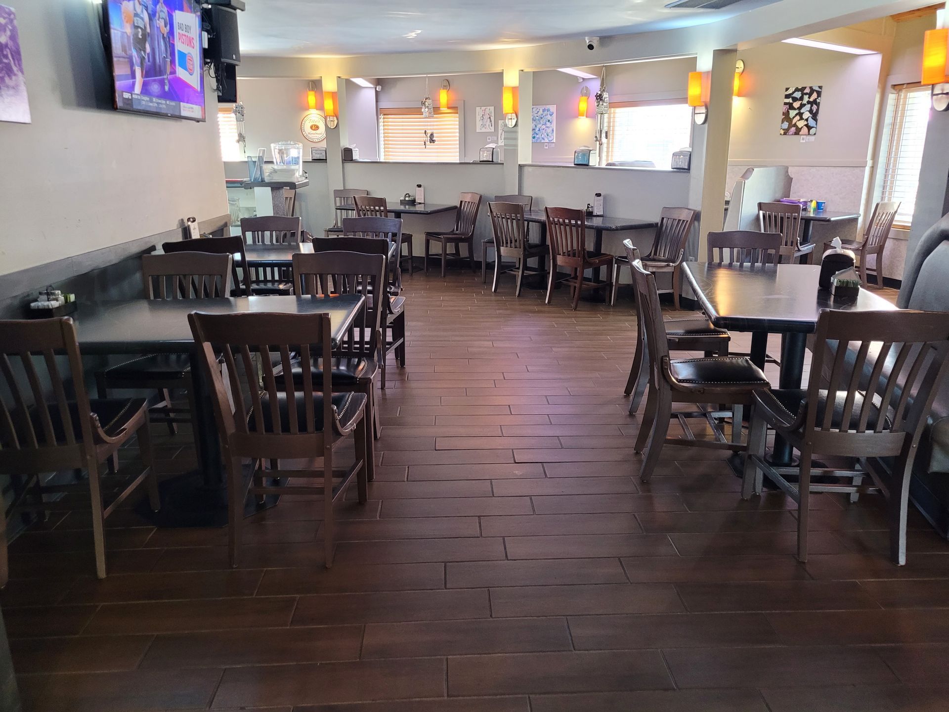 Empty restaurant dining room with wooden tables, chairs, and wall-mounted TVs.