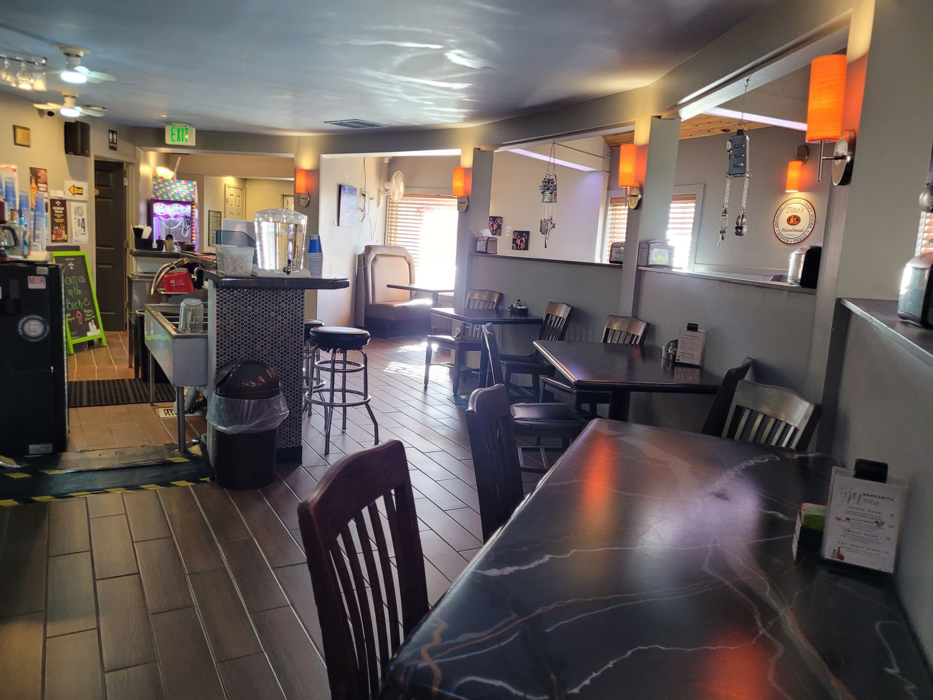 Dim restaurant interior with dark tables, bar stools, booths, and warm pendant lights