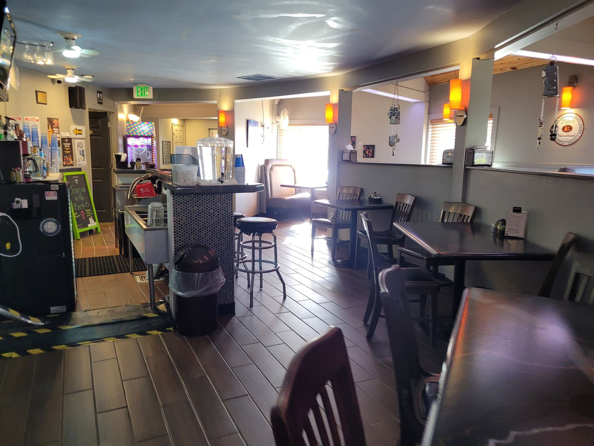 Empty café interior with dark tables, tiled floor, wall art, and warm hanging lights
