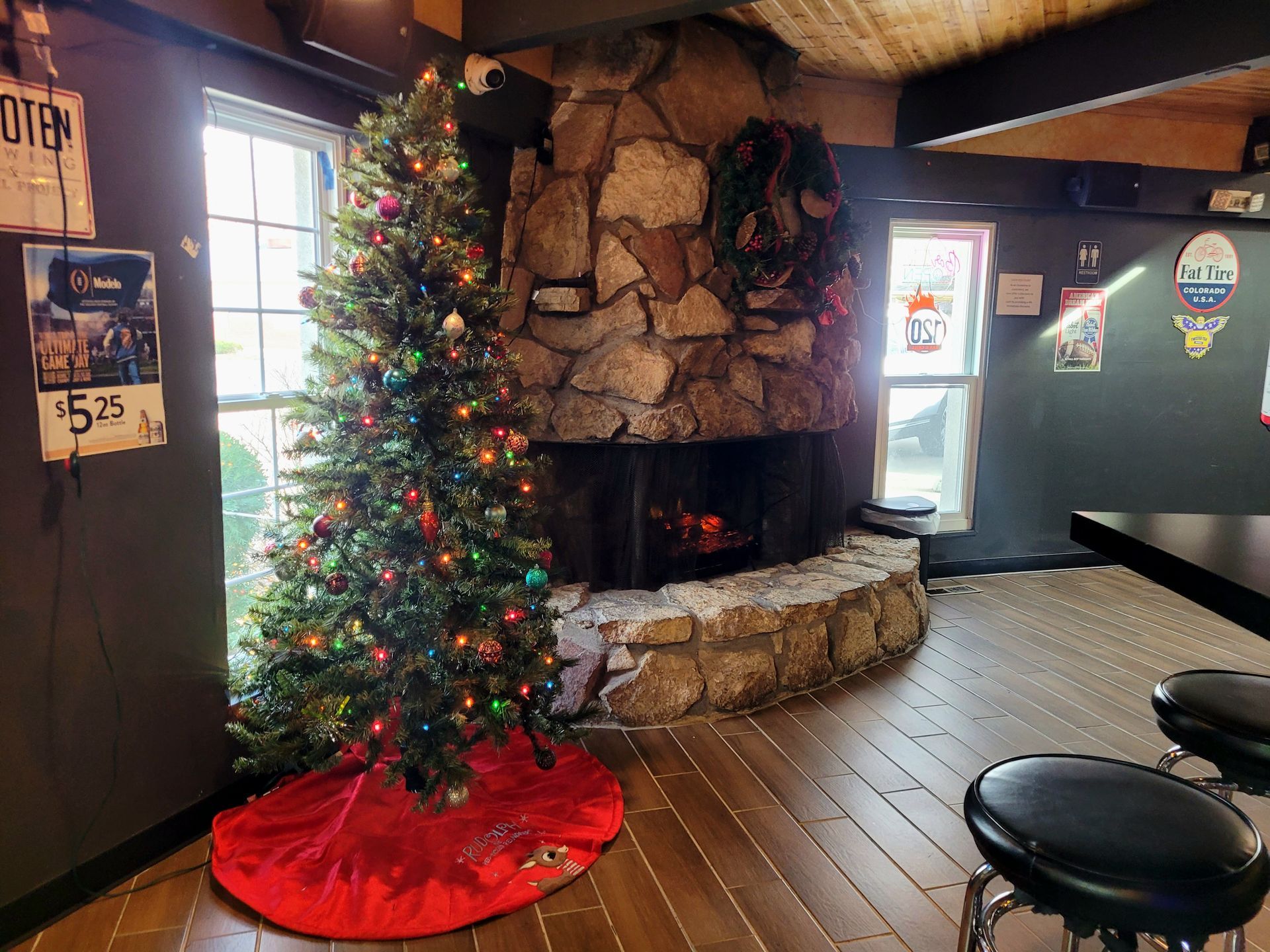 Christmas tree beside a stone fireplace in a cozy room with wooden floors and a stool