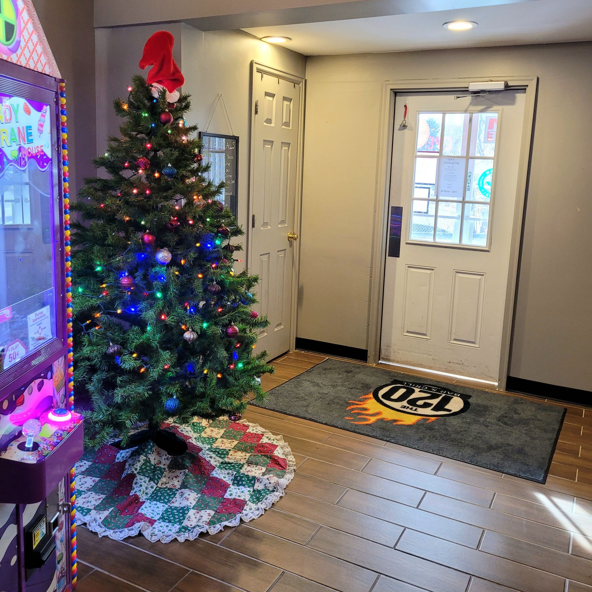 Christmas tree in a decorated entryway beside a front door with a doormat and tiled floor.