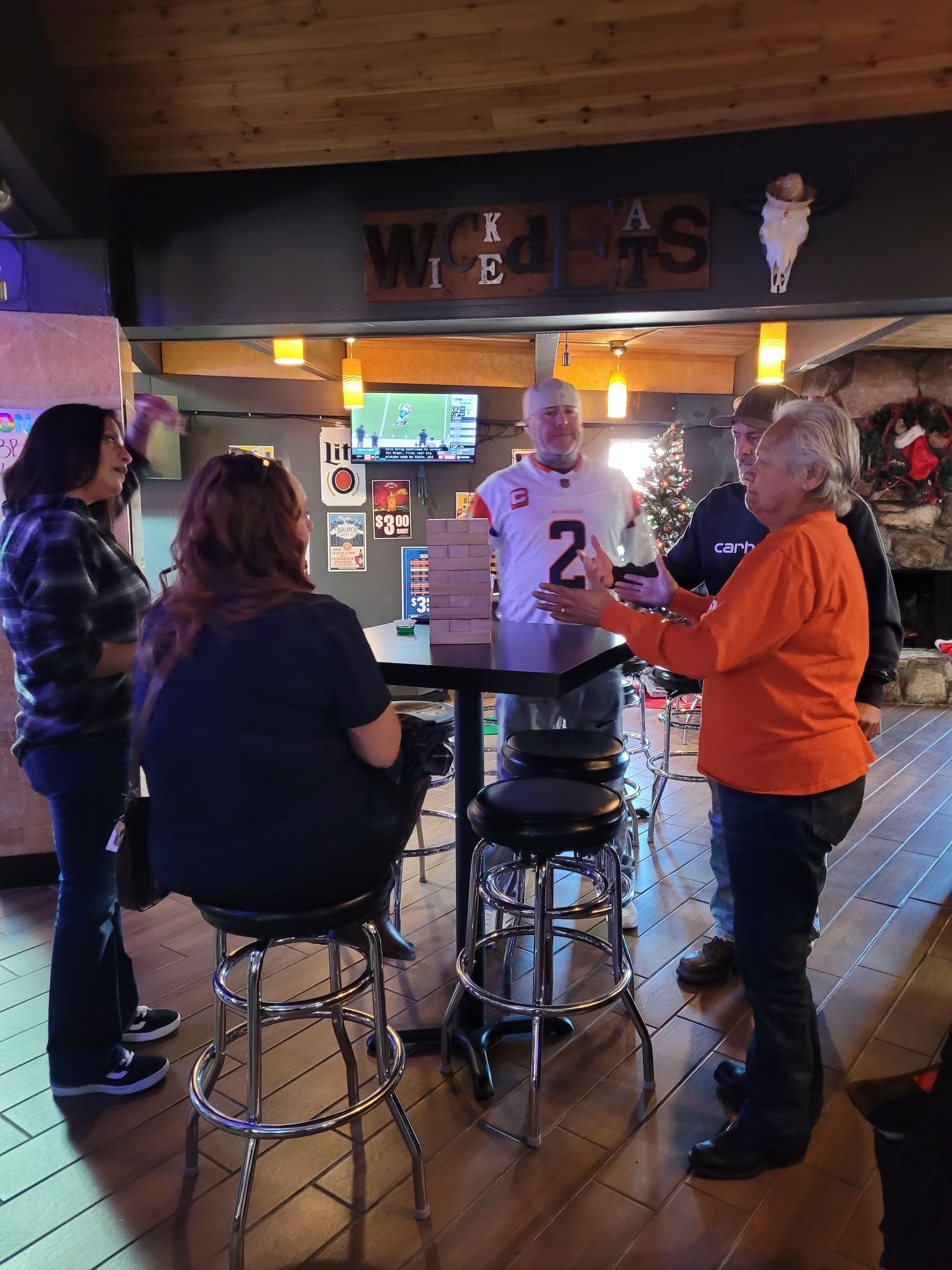 People chatting at a bar with a TV, bar stools, and Christmas lights in a cozy wooden interior