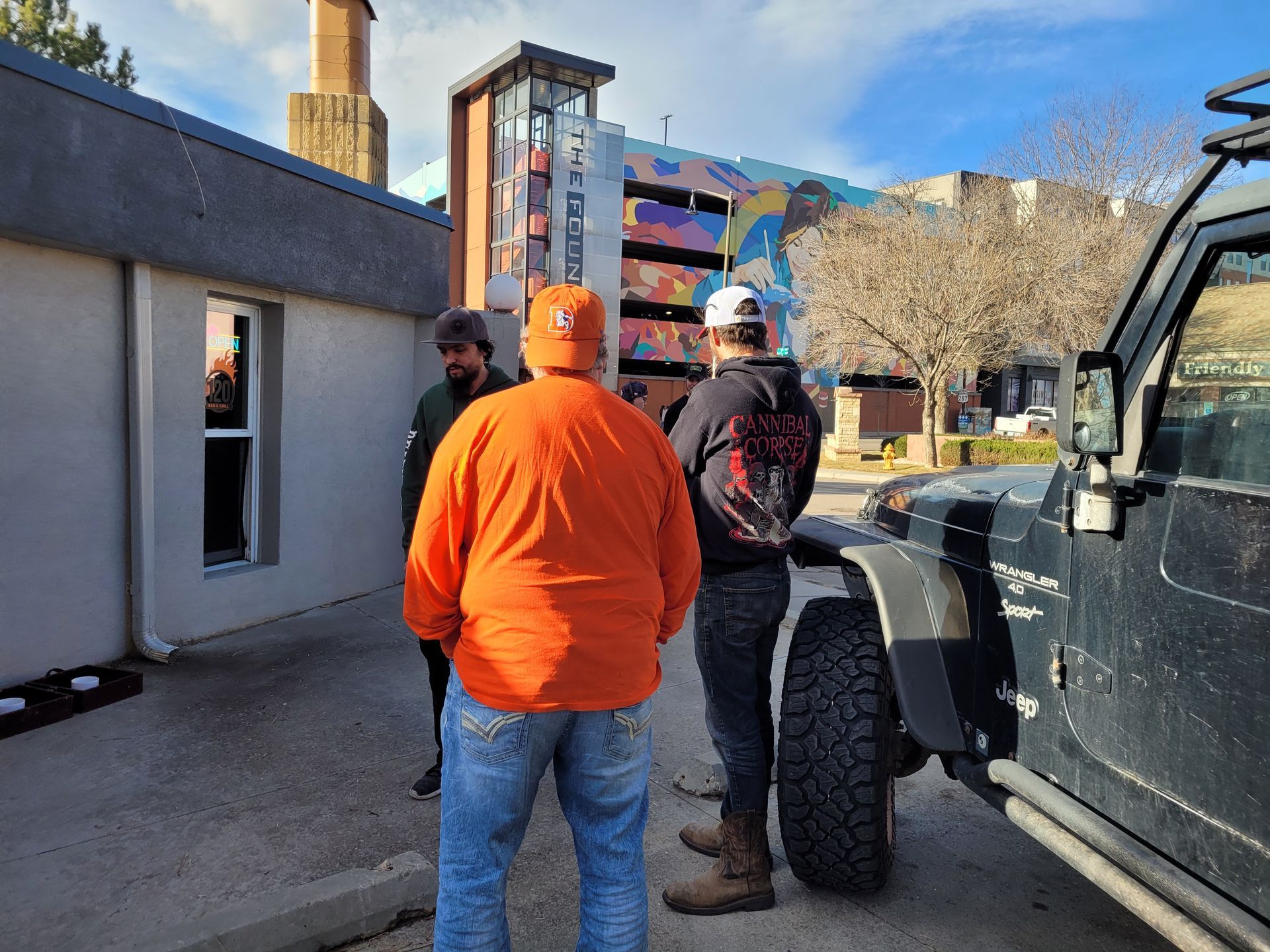 Two people in work clothes stand beside a truck, looking toward a colorful building under construction.
