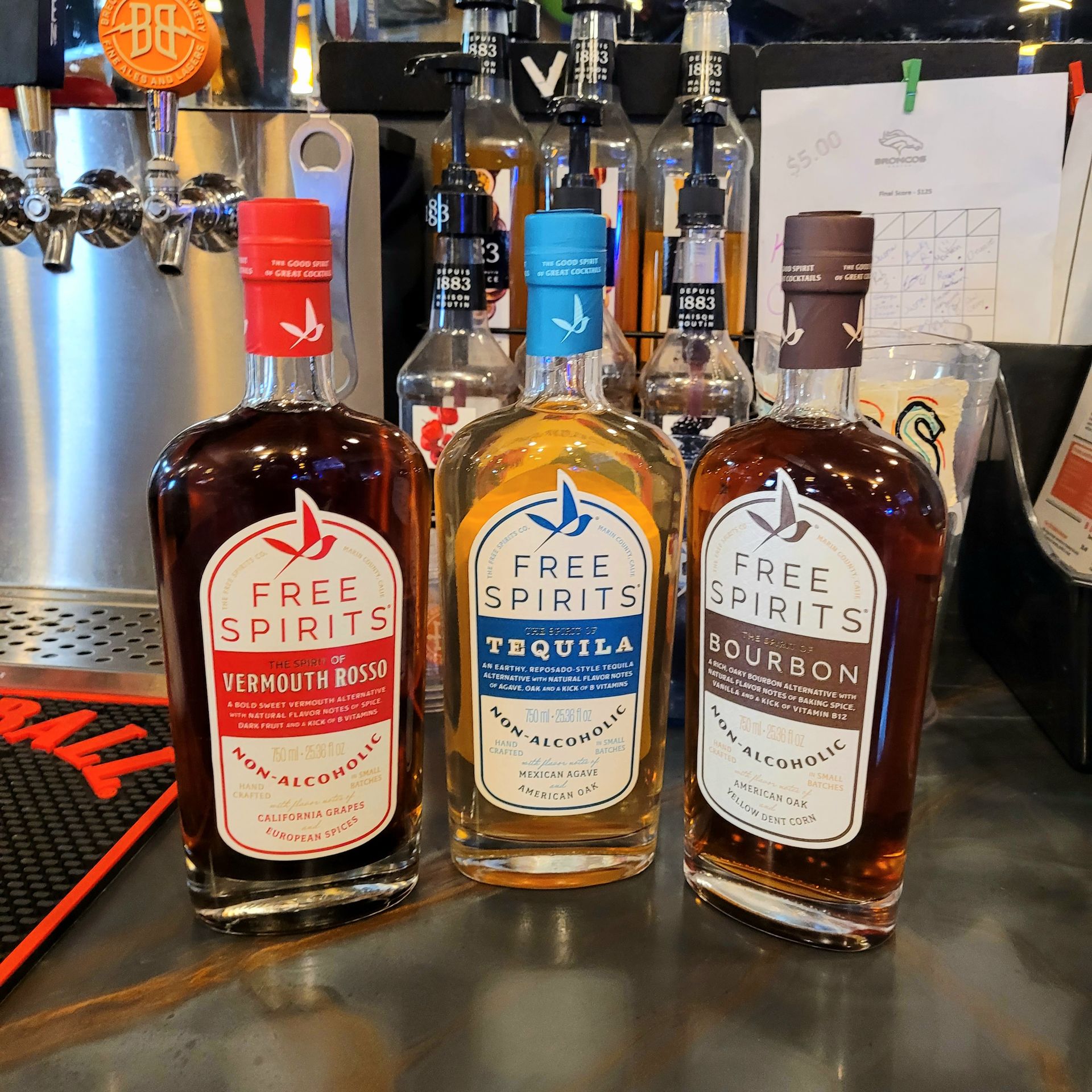 Three Free Spirits non-alcoholic bottles on a bar counter: red, blue tequila, and bourbon