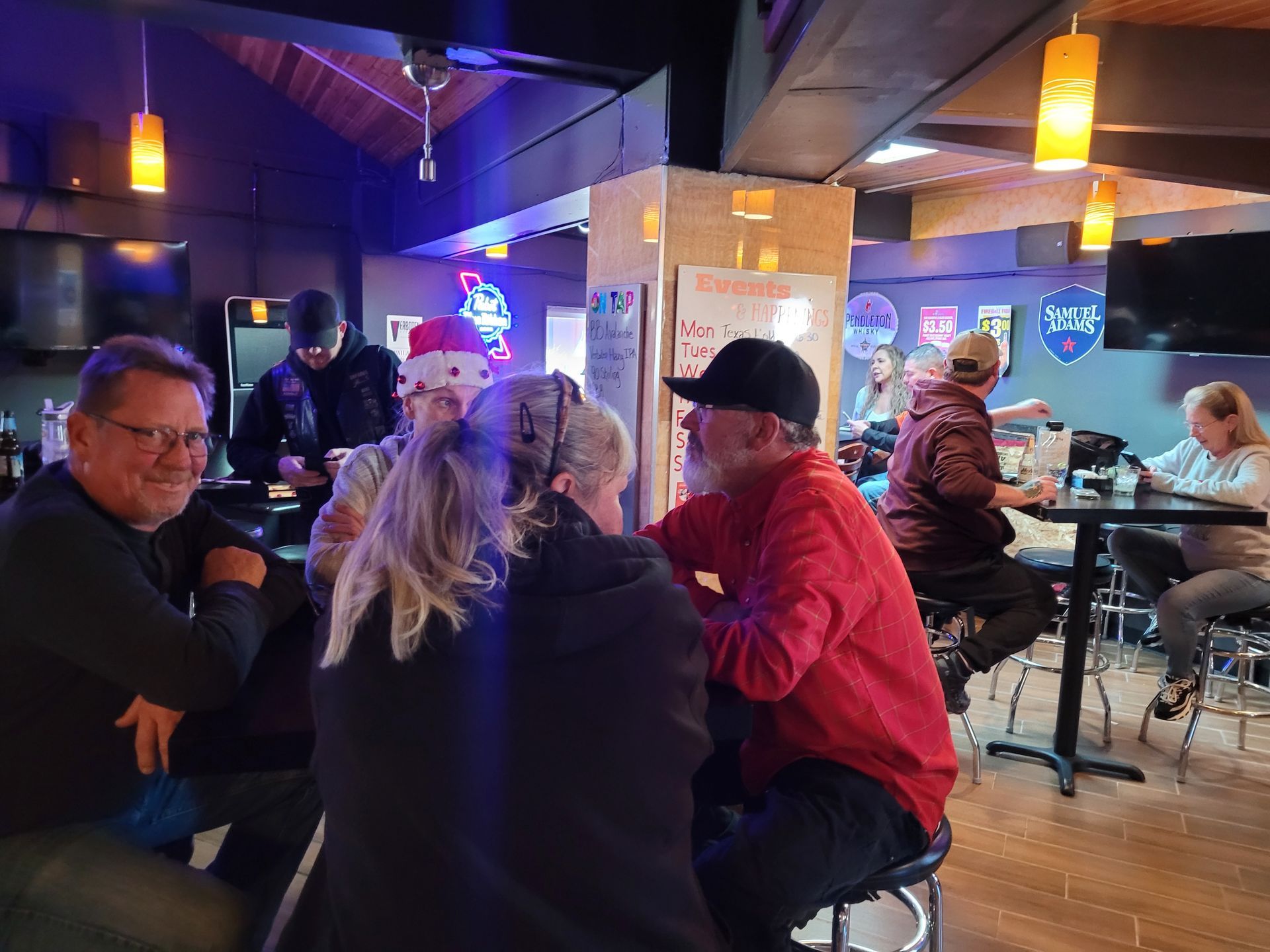 People seated at a lively bar with warm hanging lights and a TV glow in the background.