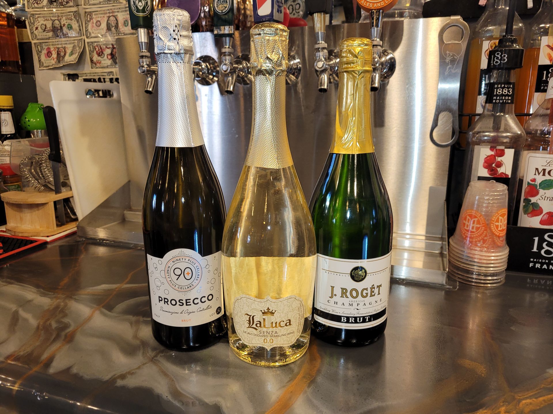 Three champagne bottles on a bar counter, with silver and gold foil tops and labels visible.