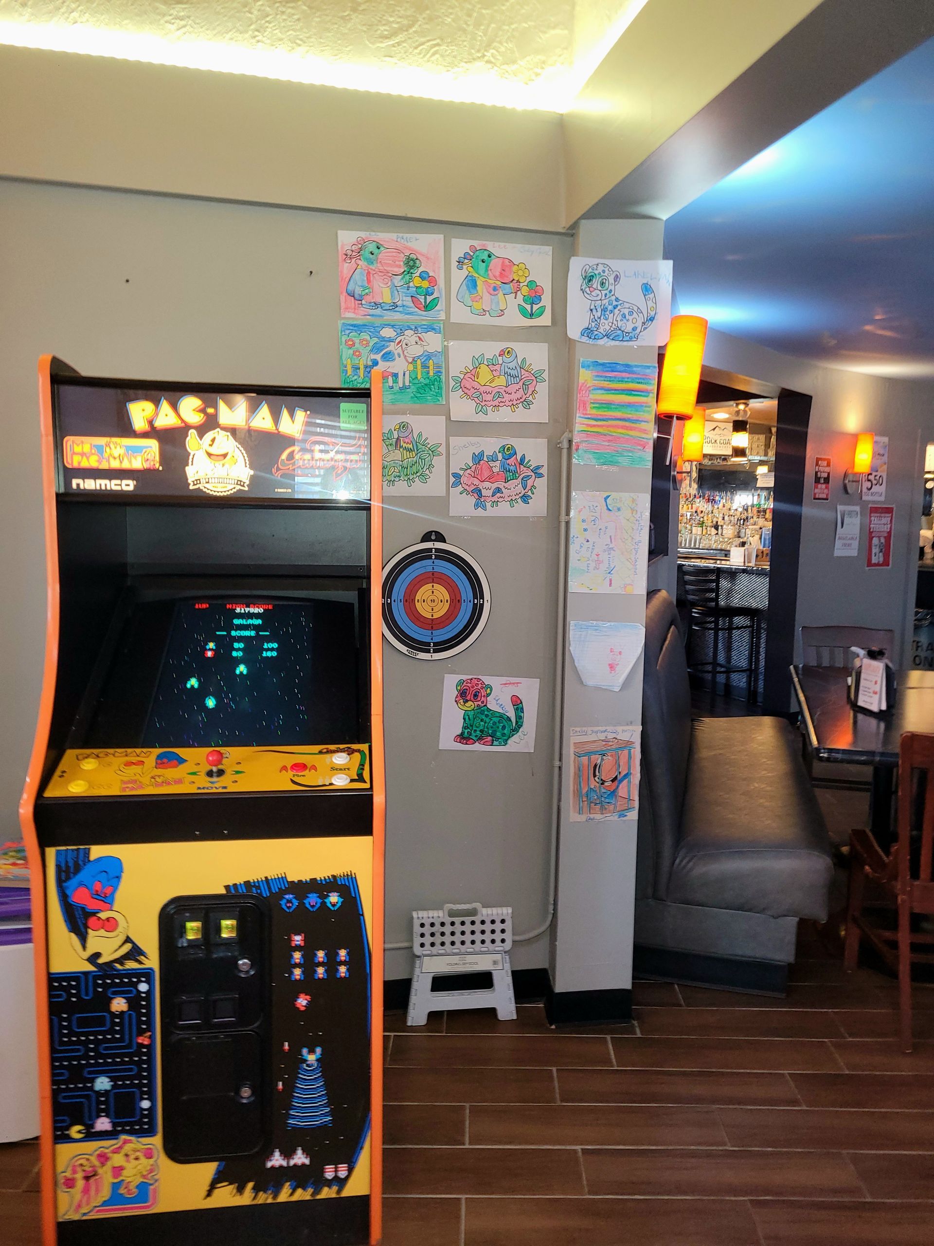 Arcade corner with a Pac-Man machine, wall art, and a stairway in a dimly lit room