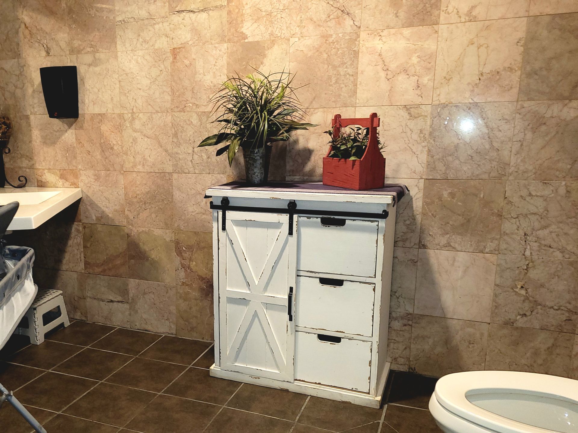 Bathroom with beige tile wall, small white cabinet, potted plant, and red decorative item.