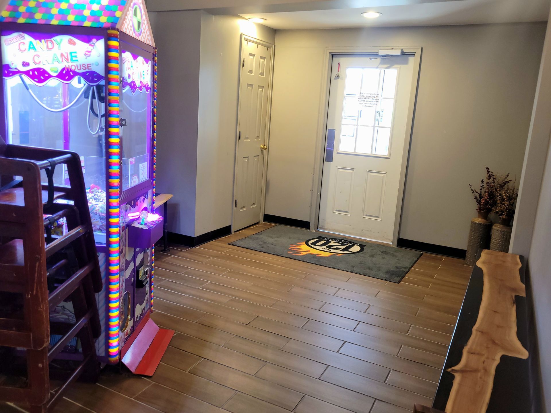 Small entryway with a white front door, wooden floor, and a glowing arcade game on the left.