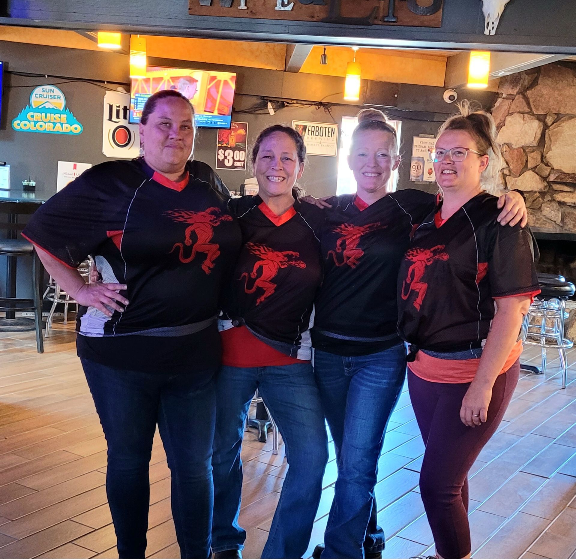 Four people in matching black-and-red tops posing together inside a bar with wood floors.