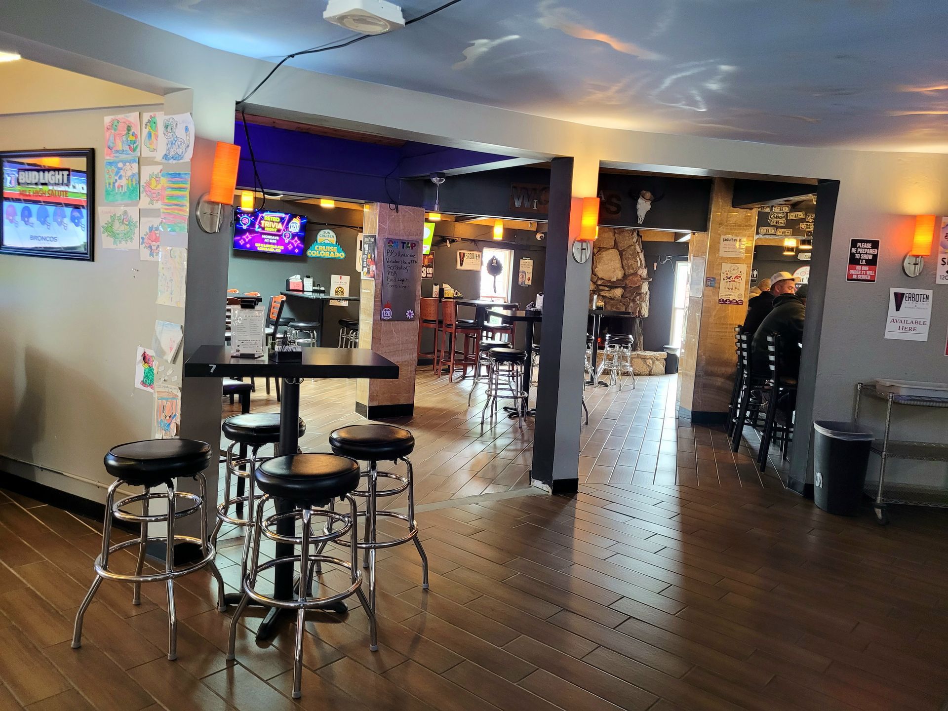 Dim arcade bar interior with high tables, stools, neon-lit games, and polished wood floors.
