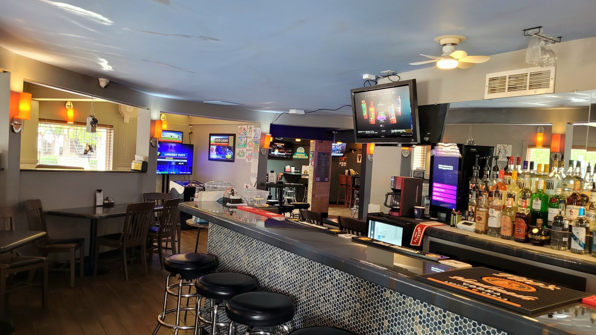 Empty bar interior with stools, TV screens, and a long counter with bottles and taps