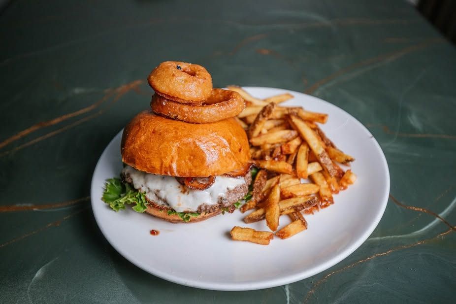 Burger with onion rings and fries on a white plate on a green table