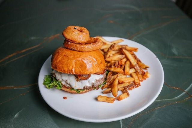 Burger with lettuce and sauce on a white plate, served with a side of seasoned fries.