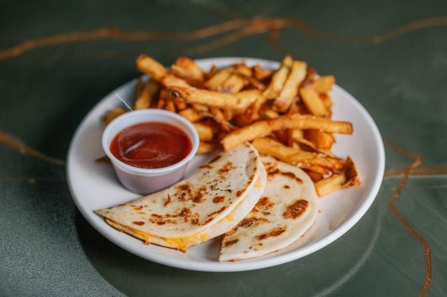 Quesadilla slices, fries, and ketchup in a white plate on a dark table