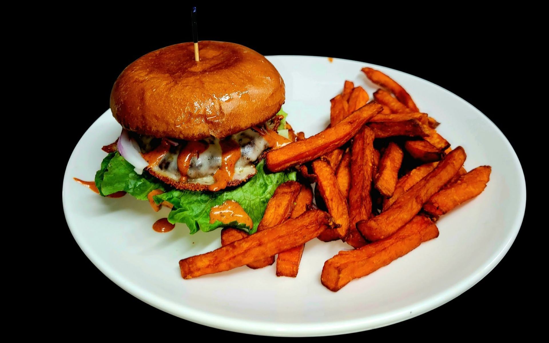 Burger and fries on a white plate, with a glazed bun and golden brown fries.