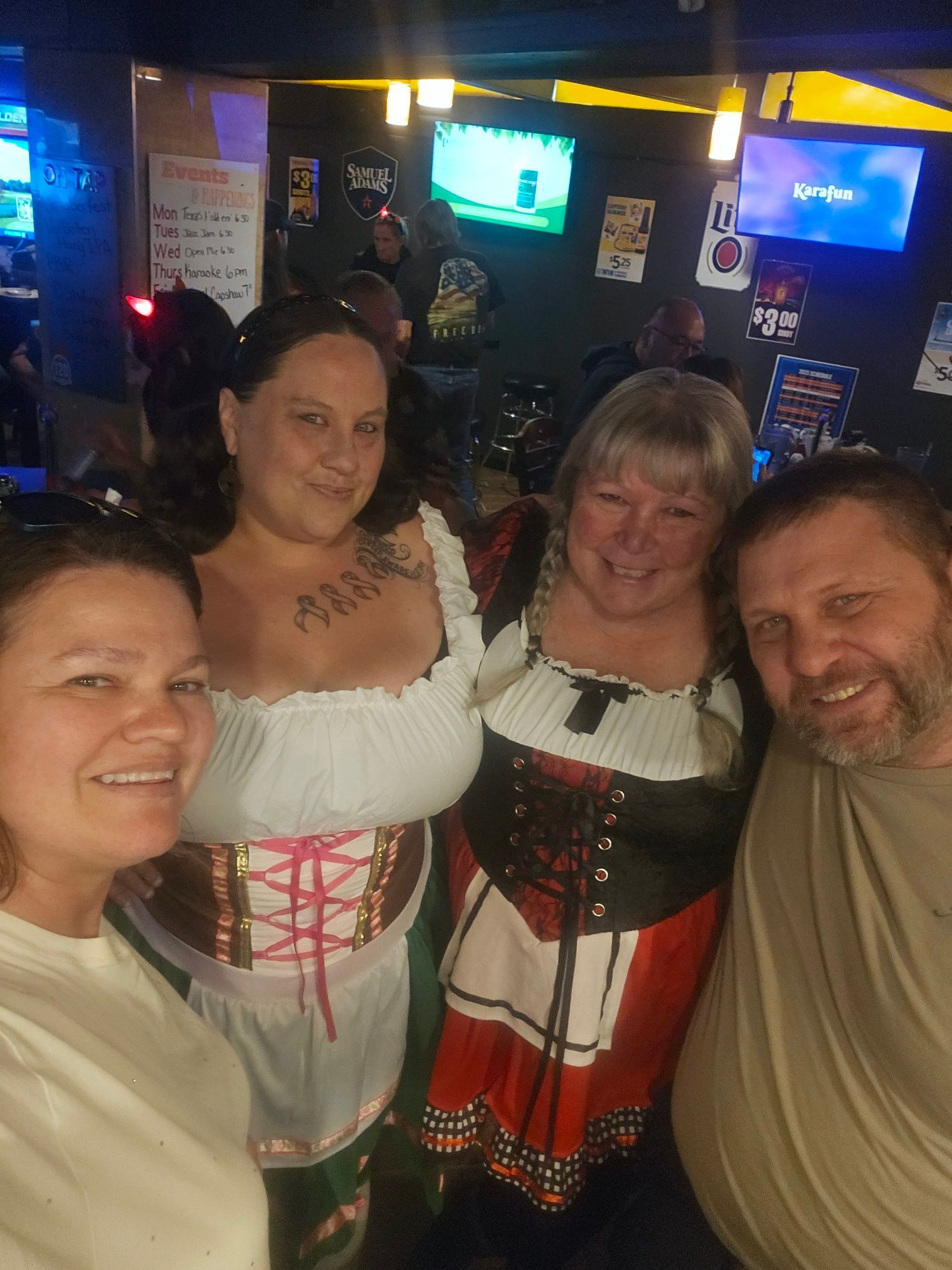 Four people smiling in traditional-style dresses inside a dimly lit bar.