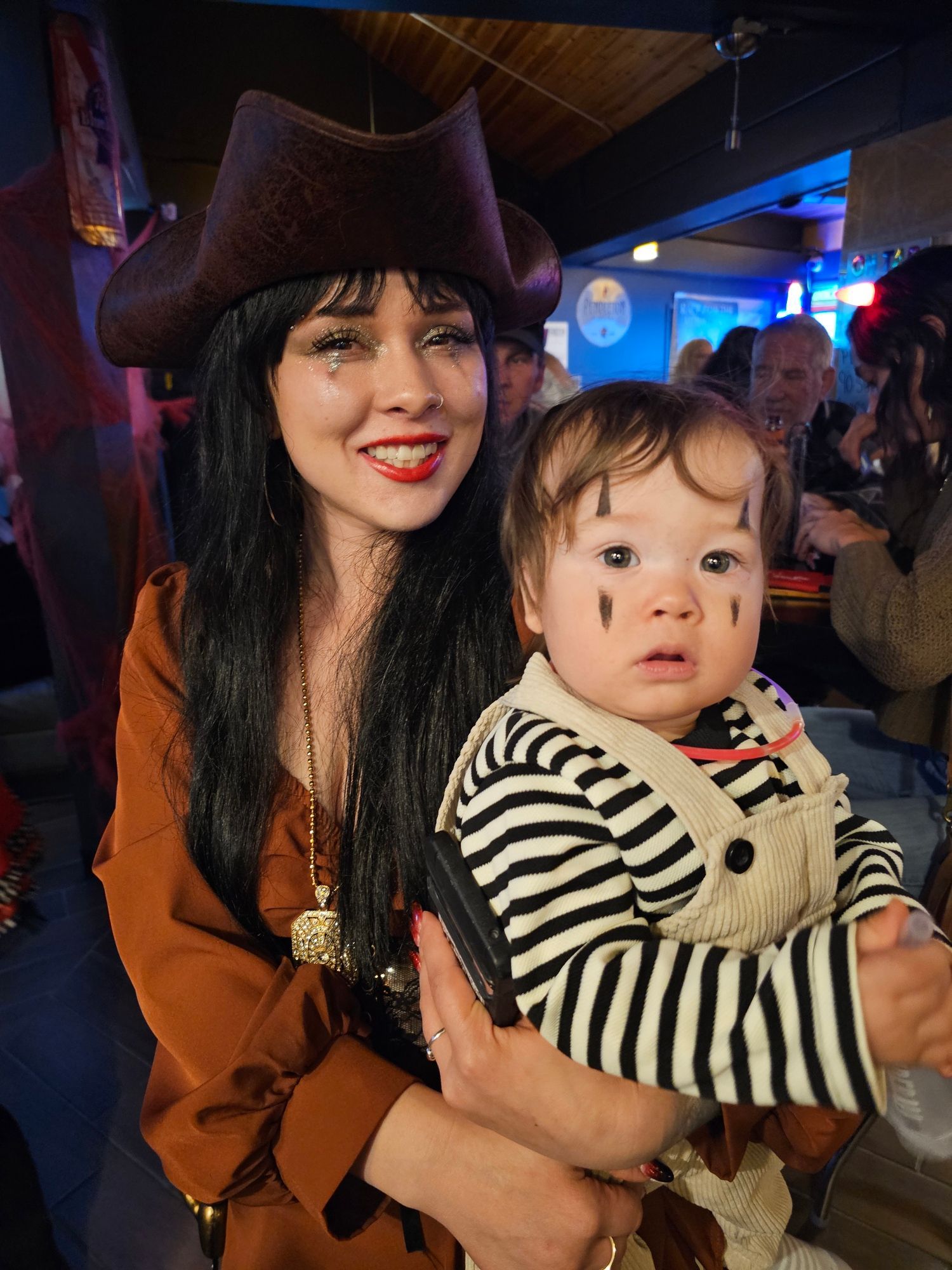 Woman in a brown hat holding a child in a striped shirt at a dimly lit indoor event