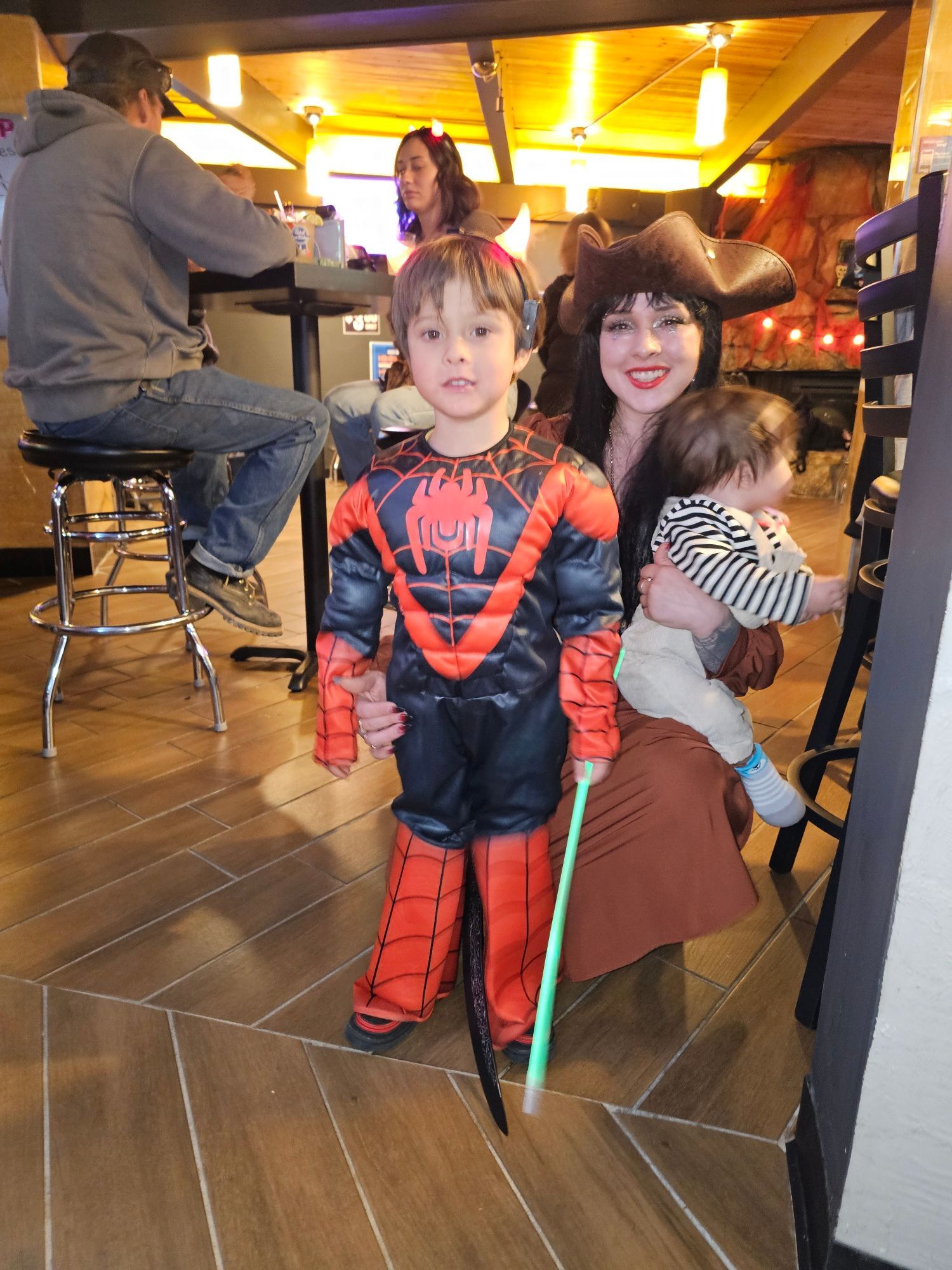 Two children in Halloween costumes posing in a warmly lit restaurant, one holding a baby.