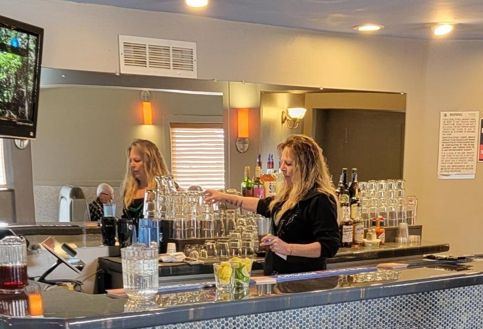 Two bartenders working behind a bar with rows of glasses and bottles in a warmly lit lounge