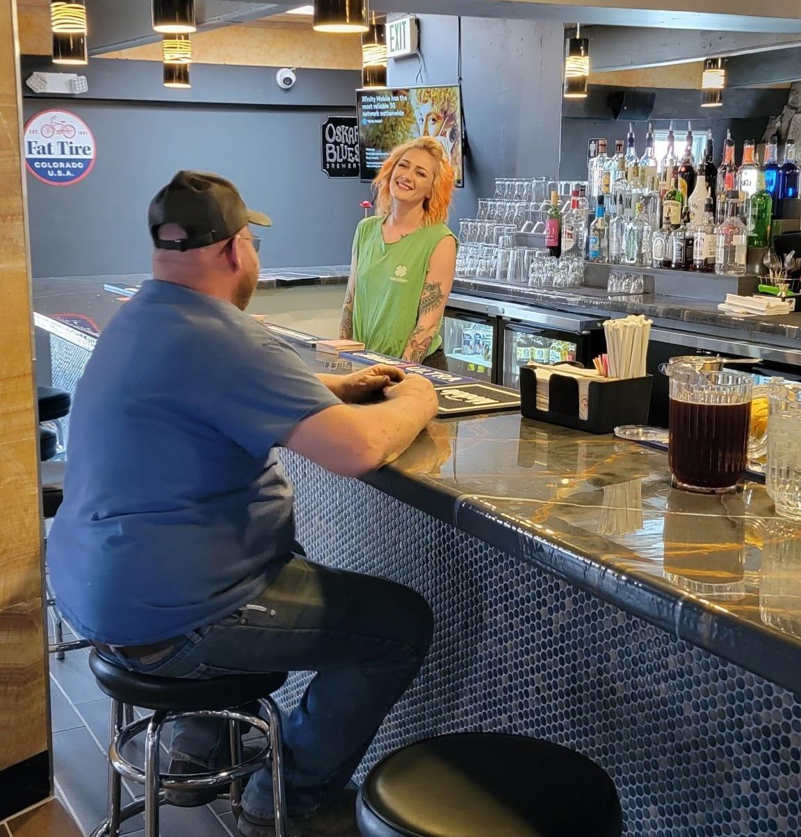 Man seated at a bar chatting with a smiling bartender in a dimly lit restaurant.