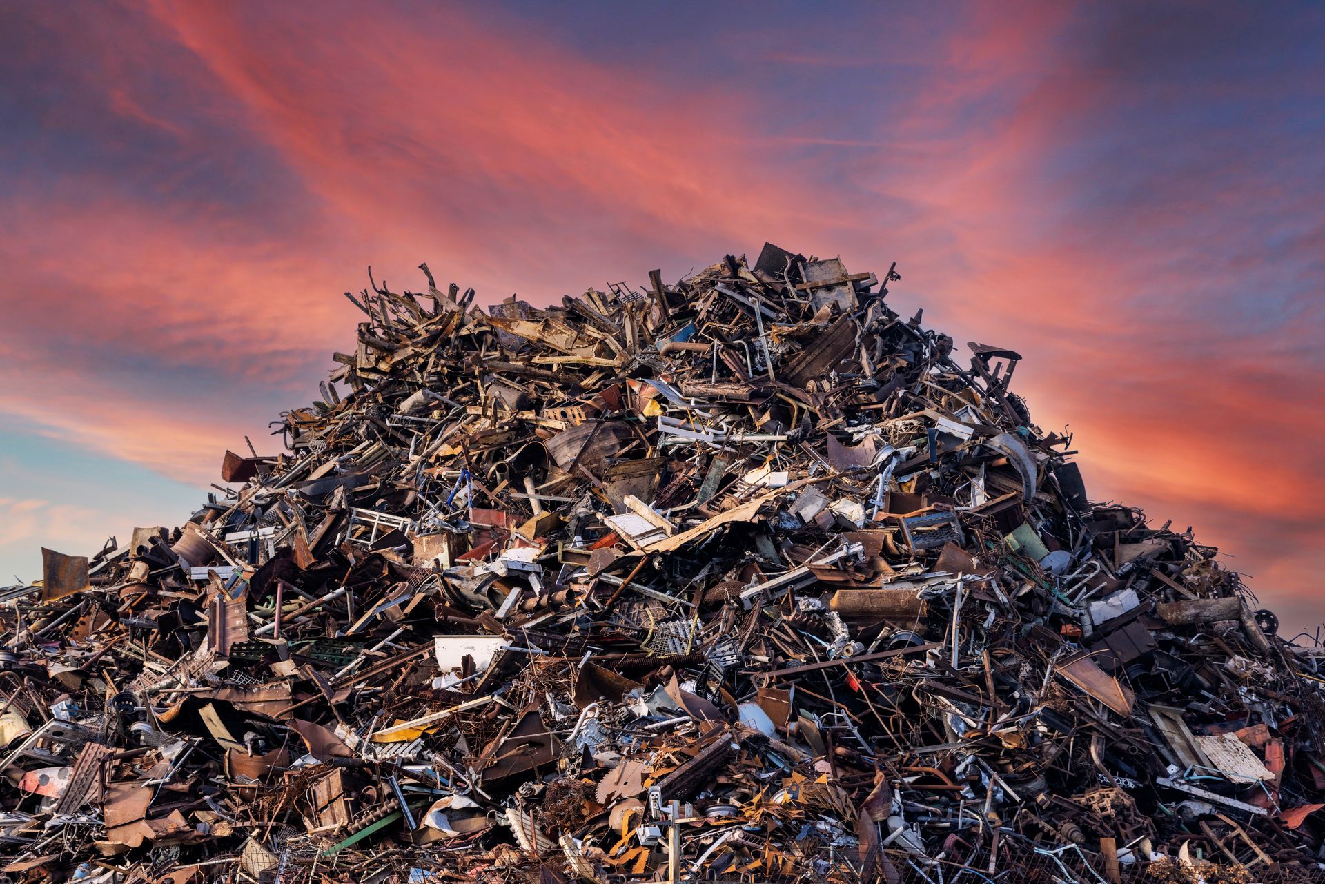 Large pile of scrap metal and debris under colorful sunset sky. Large pile of scrap metal and debris under colorful sunset sky.