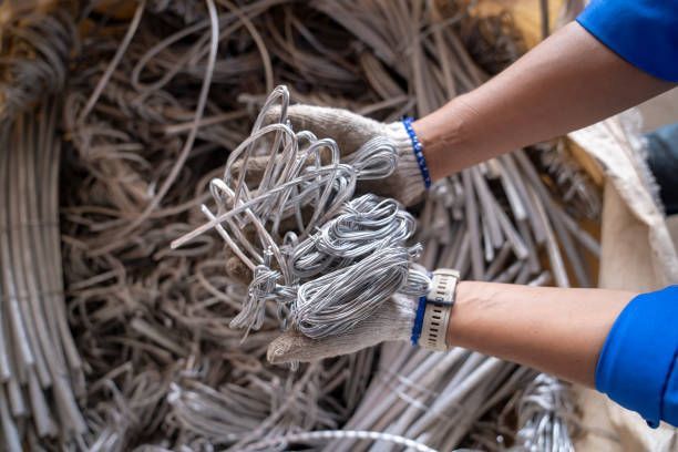 Portrait of worker with gloved hands, standing in front of scrap in a metal recycling facility.
