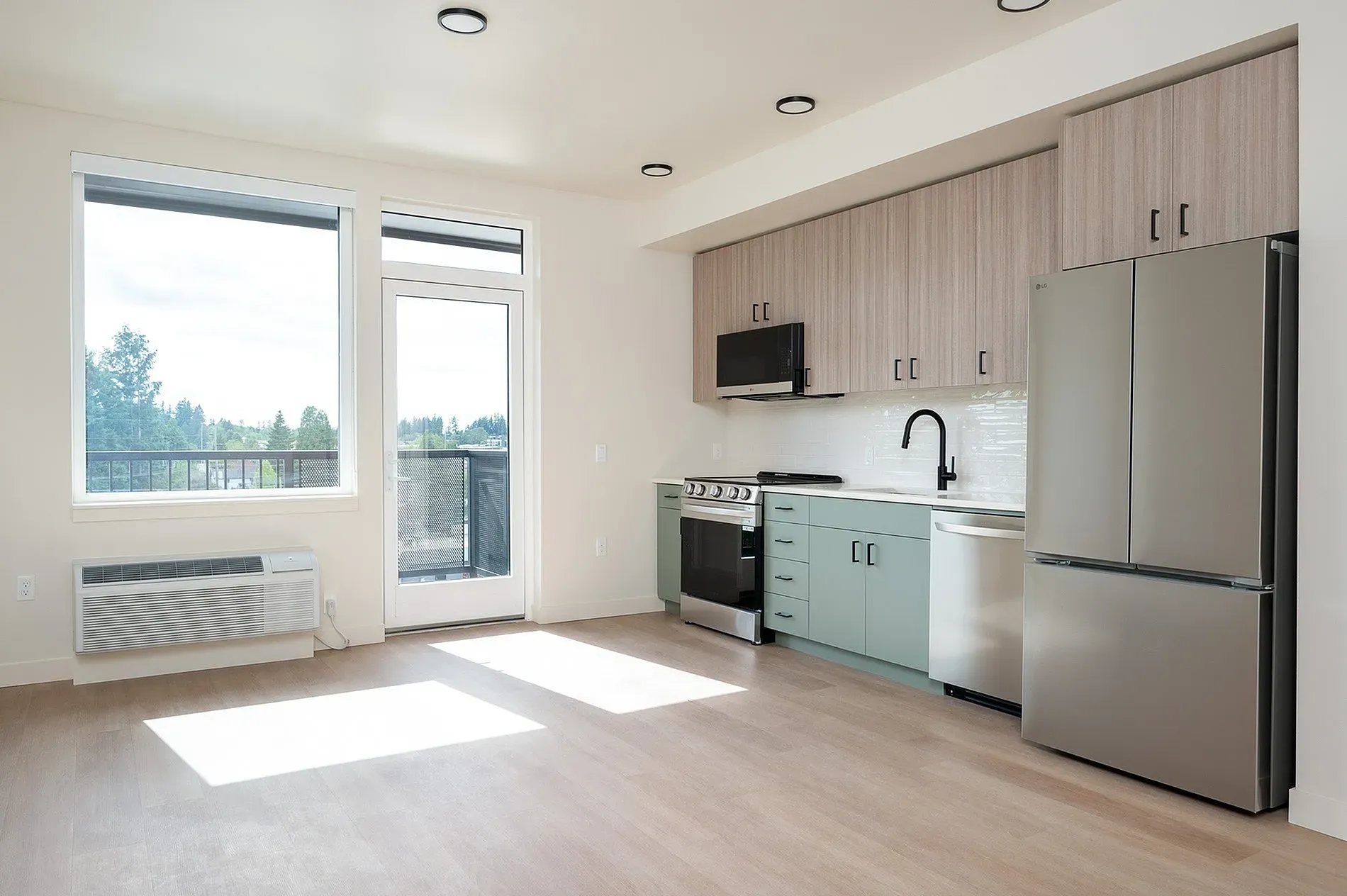 Modern kitchen with light wood cabinets, sage green lower cabinets, stainless steel appliances, and a large window.