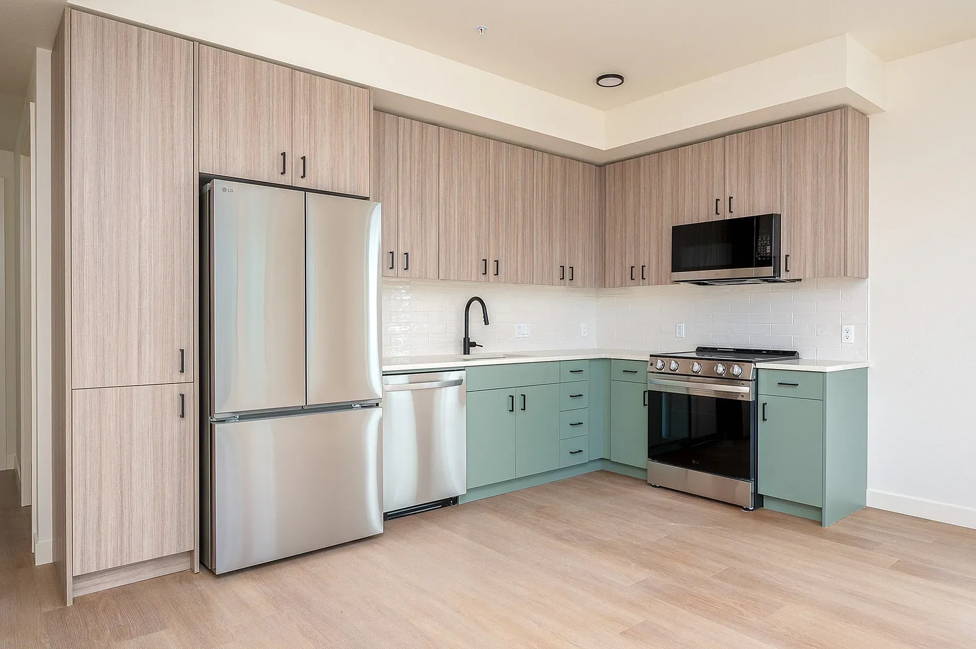 Modern kitchen with stainless steel appliances, light wood cabinets, and mint green lower cabinets.