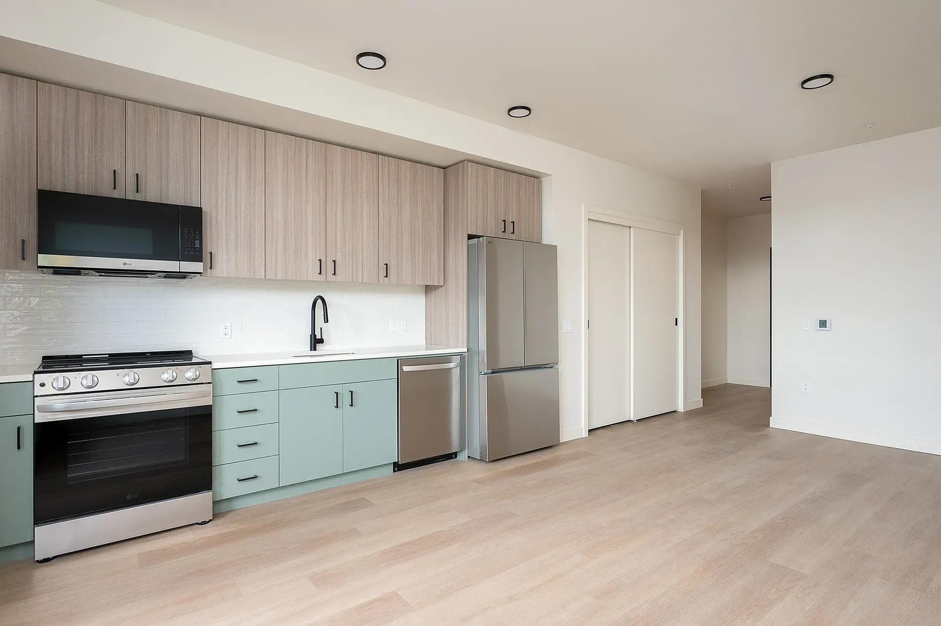 Modern kitchen with light wood cabinets, teal lower cabinets, stainless steel appliances, and subway tile backsplash.